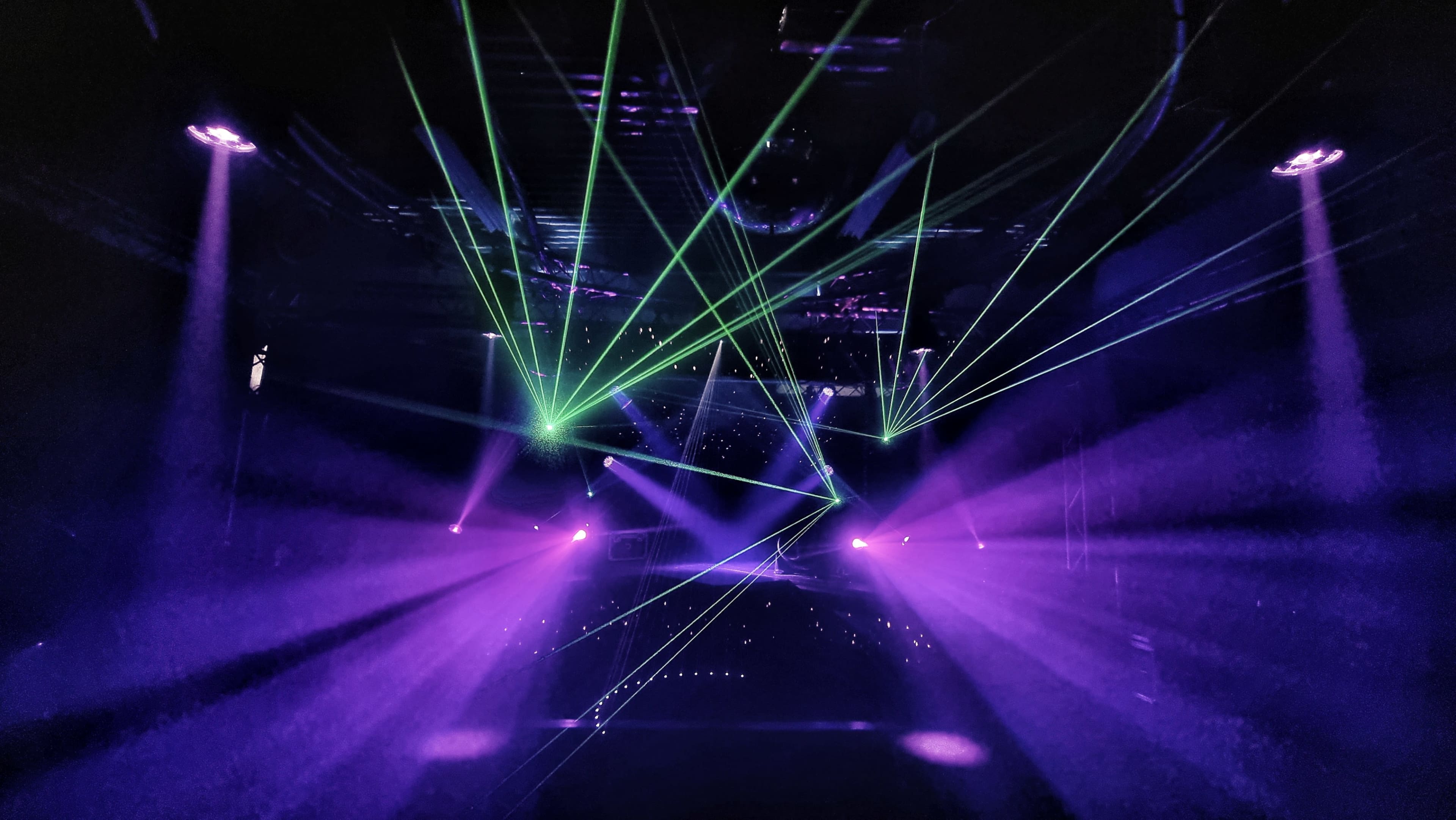 A dark venue illuminated by vibrant laser beams in green and purple, creating a dynamic light display.