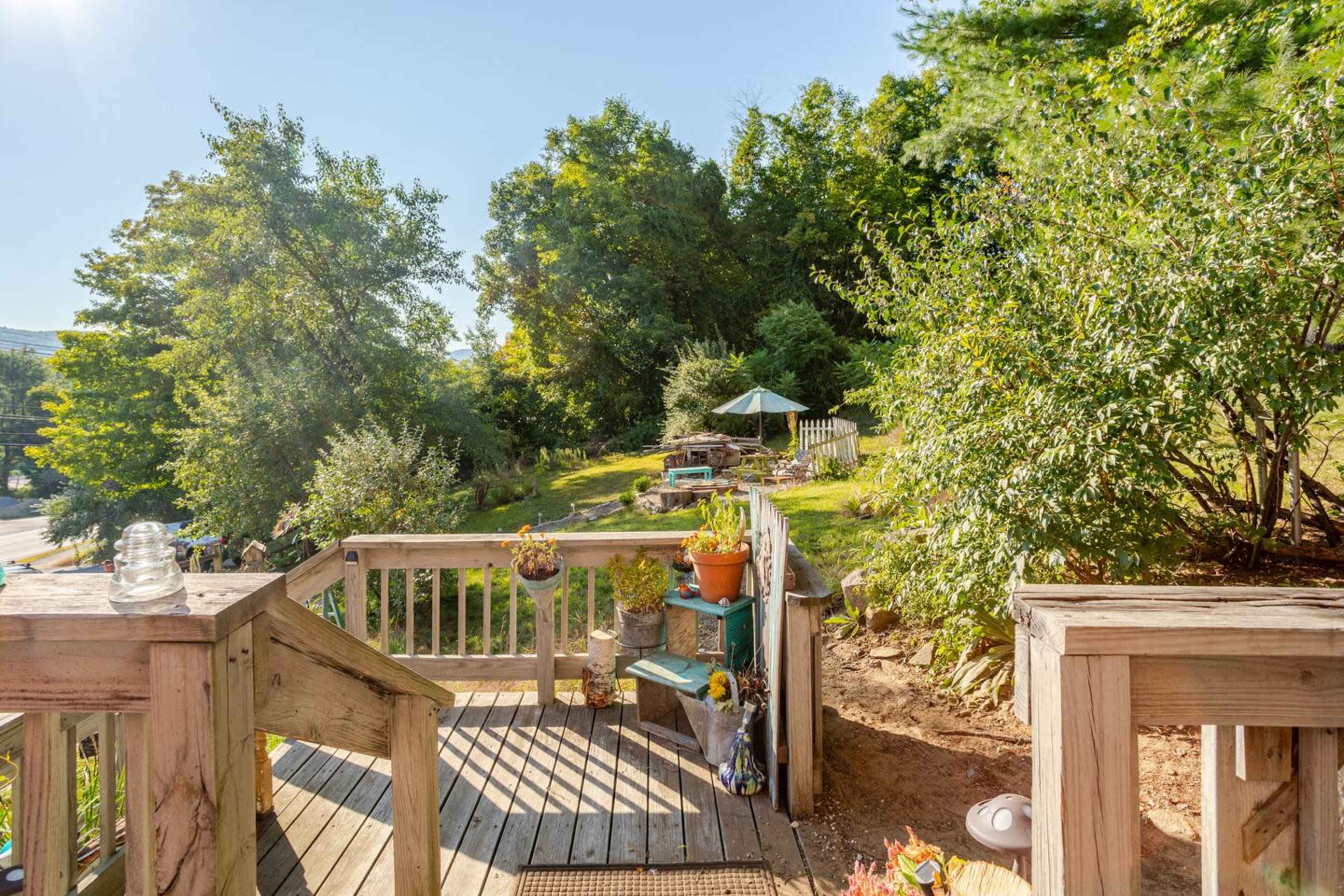 The image shows a wooden deck leading down to a sloped, green area with trees and shrubs, along with garden decorations.