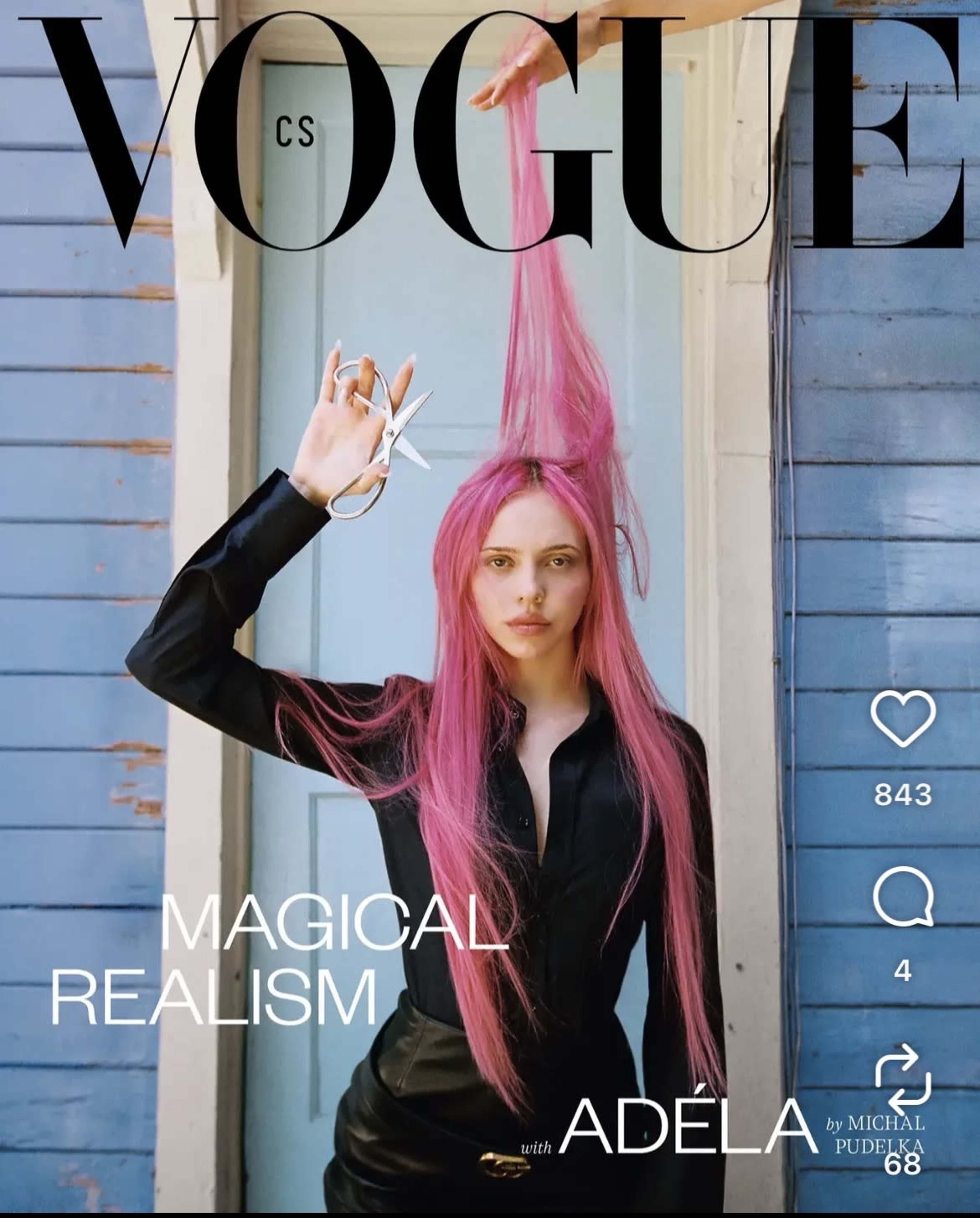 A young woman with long pink hair holds a pair of scissors in front of a blue wooden wall.