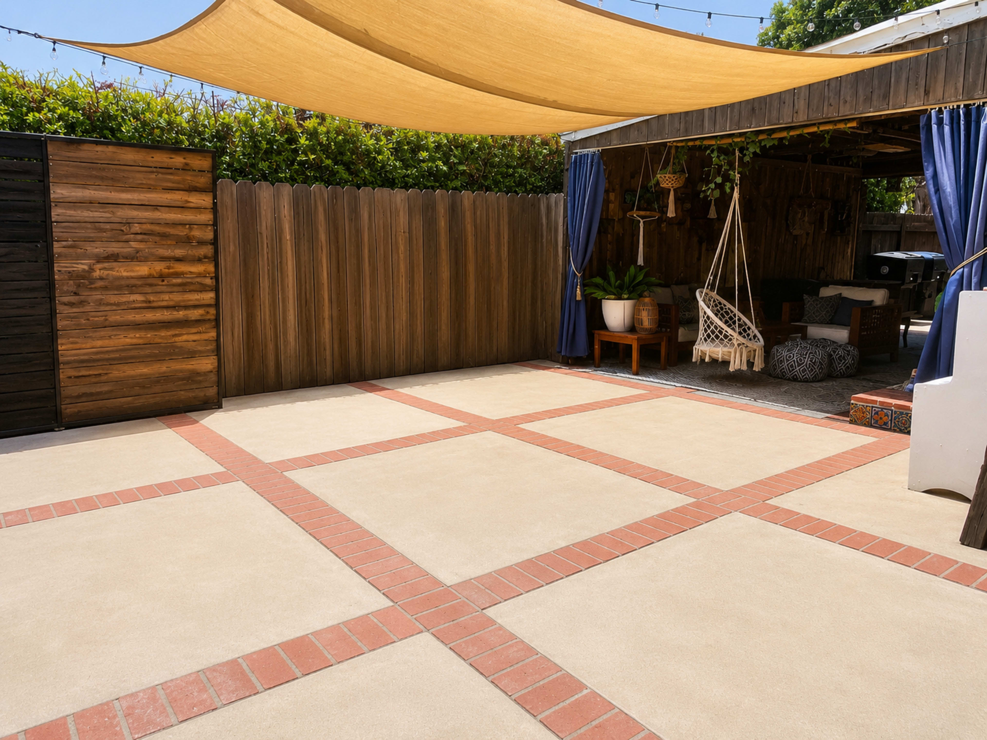 The image shows a patio area with a shaded section, featuring a concrete floor with brick patterns and wooden fencing in the background.