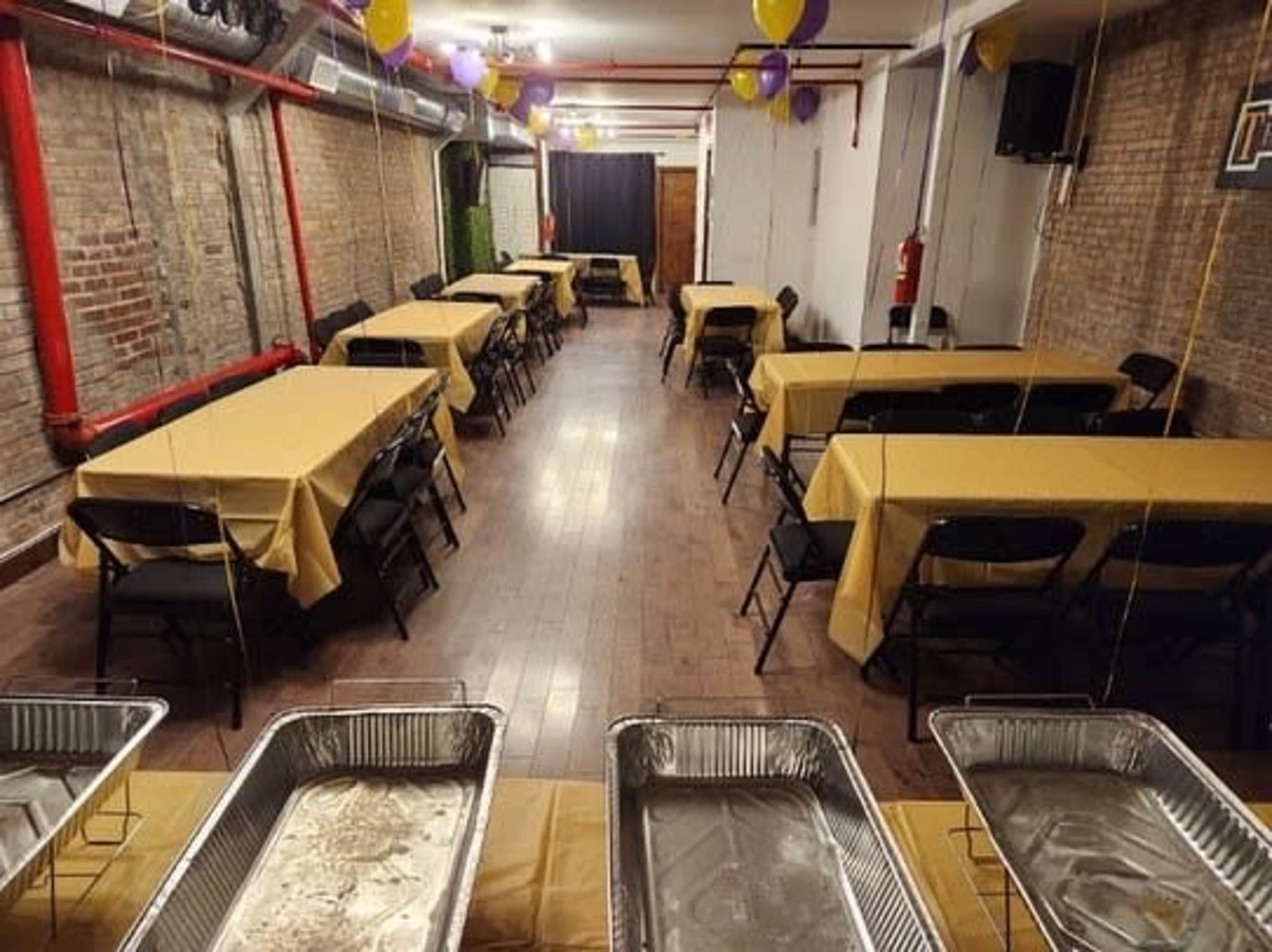 A banquet hall arranged with several tables covered in yellow tablecloths and catering trays in the foreground.