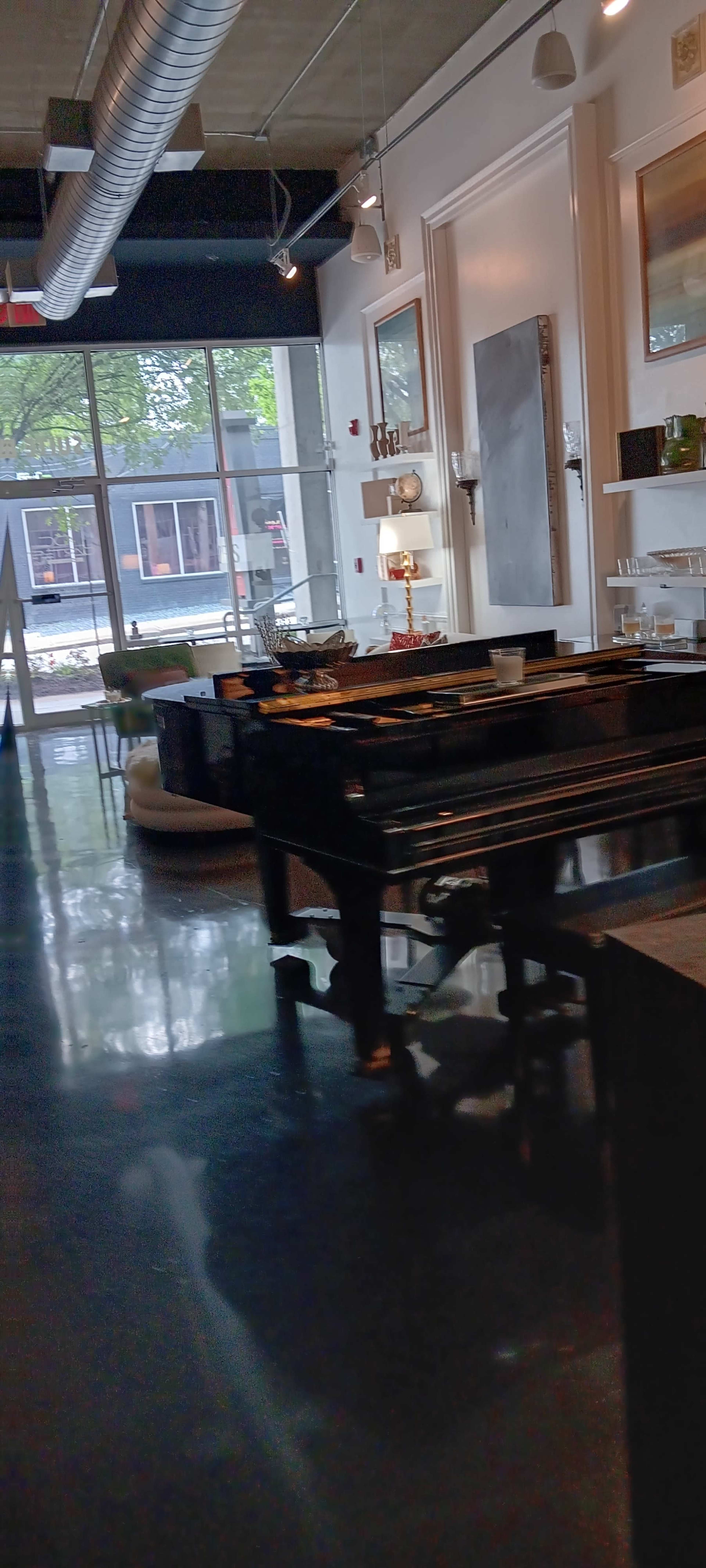 A grand piano is positioned in a modern room with large windows that provide a view of the street outside.