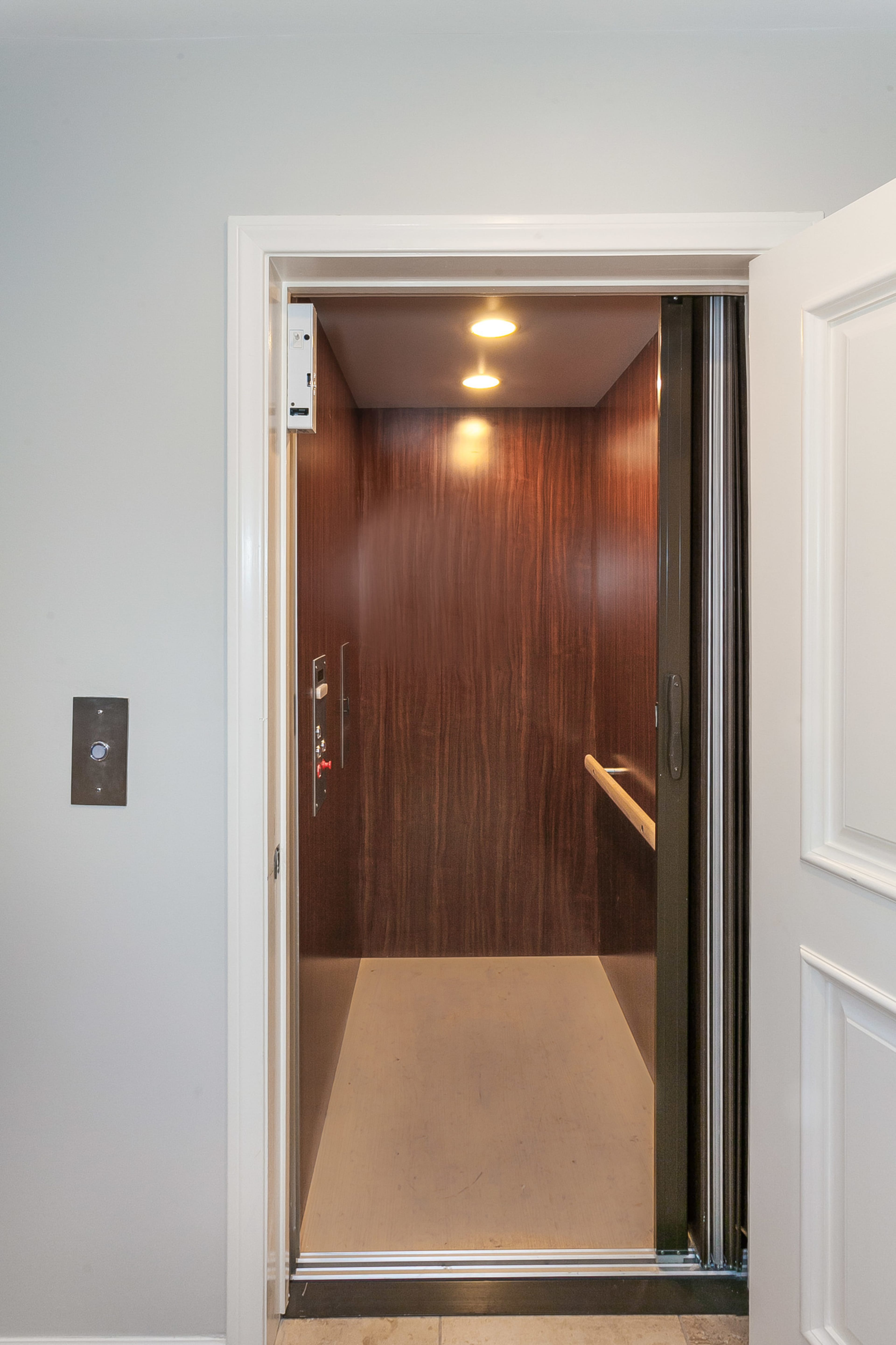 An open elevator with wooden paneling and lights overhead is shown from the doorway.