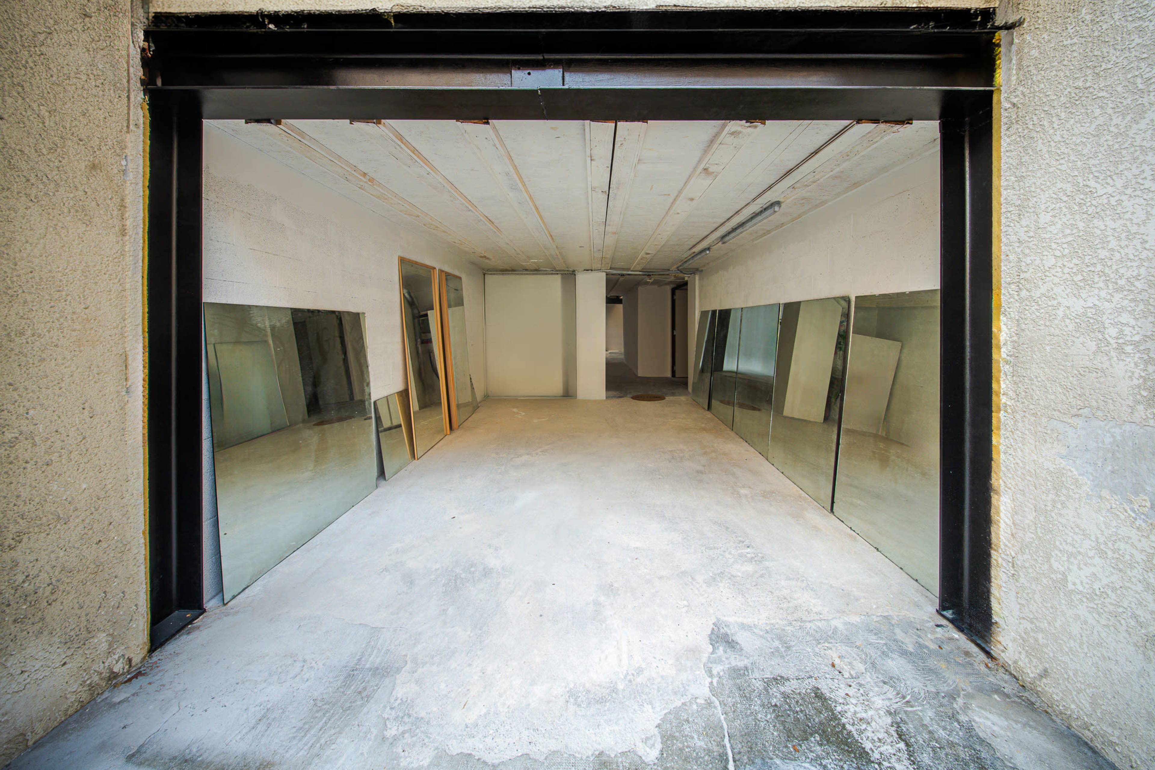 The image shows an empty garage space with large glass panels leaning against the walls.