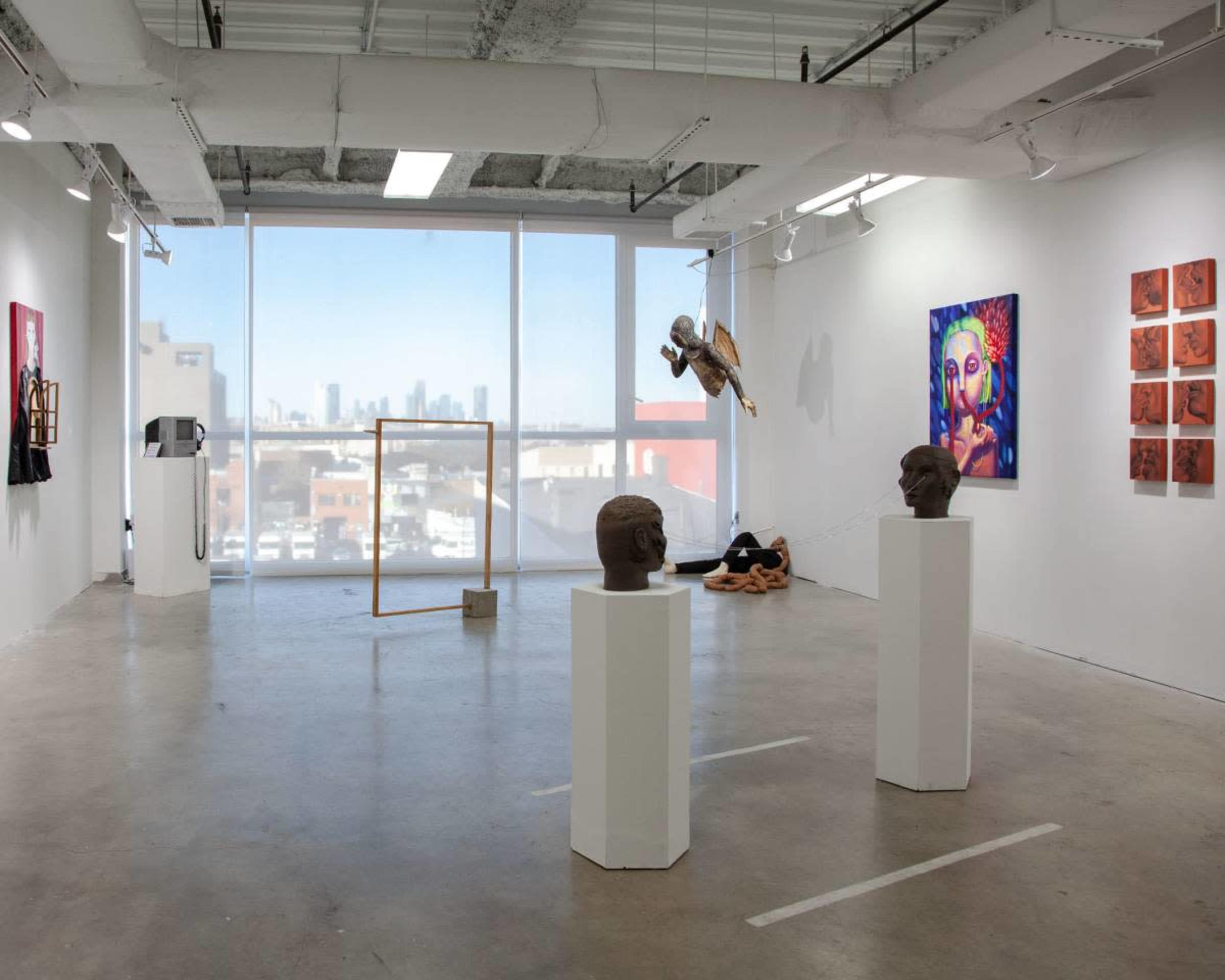 The image shows an art gallery featuring sculptures on pedestals, colorful wall art, and large windows overlooking a cityscape.