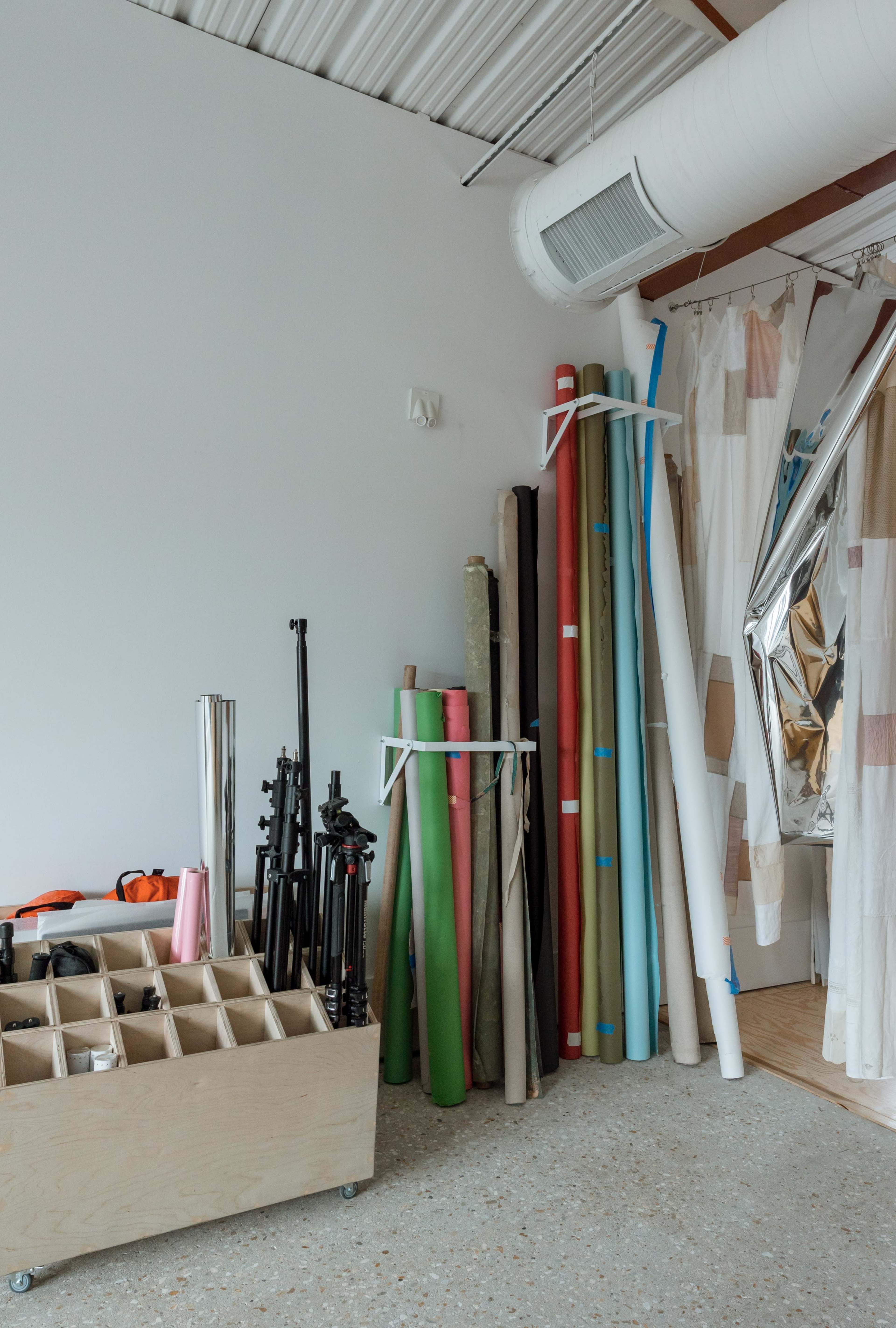 A storage area features various rolls of colored paper and equipment, organized against a wall in a studio space.