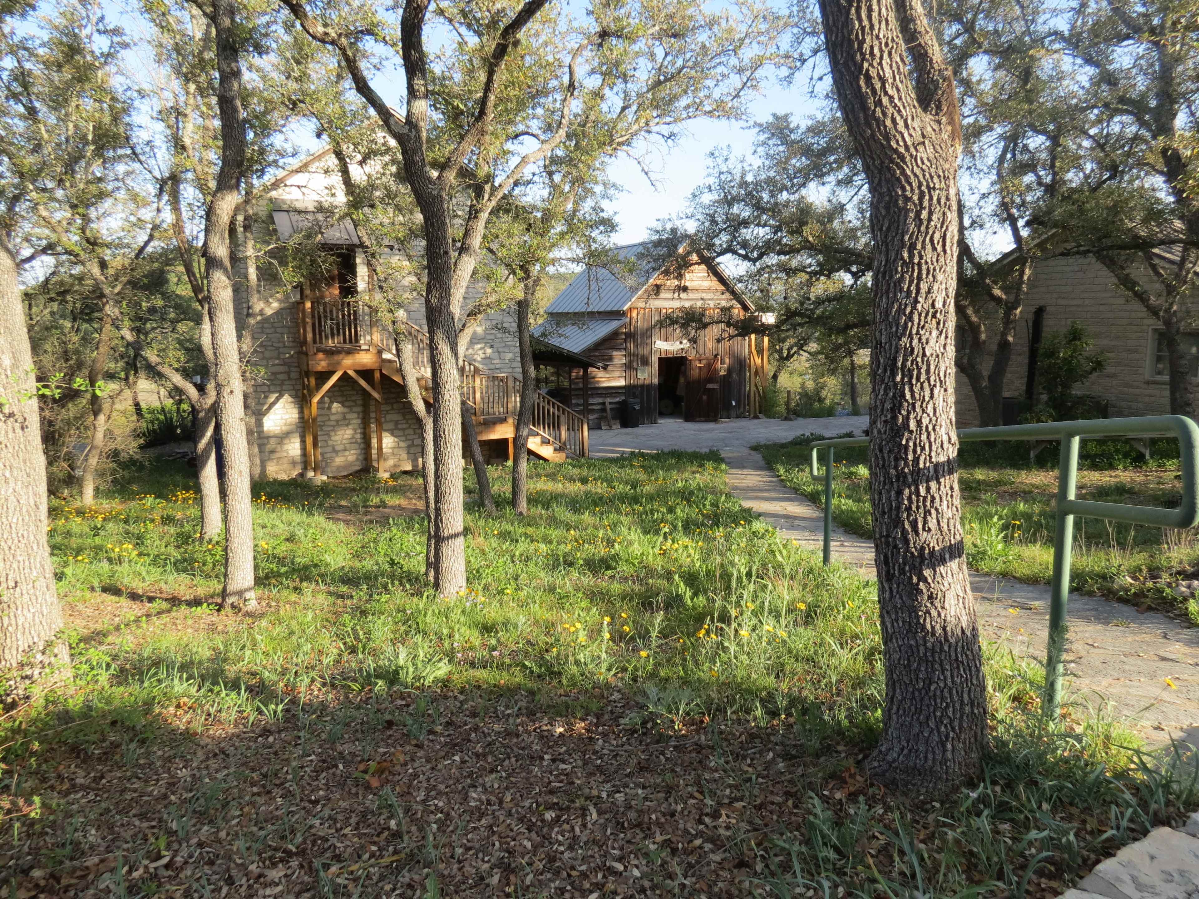 A pathway leading to two rustic buildings surrounded by trees and greenery.