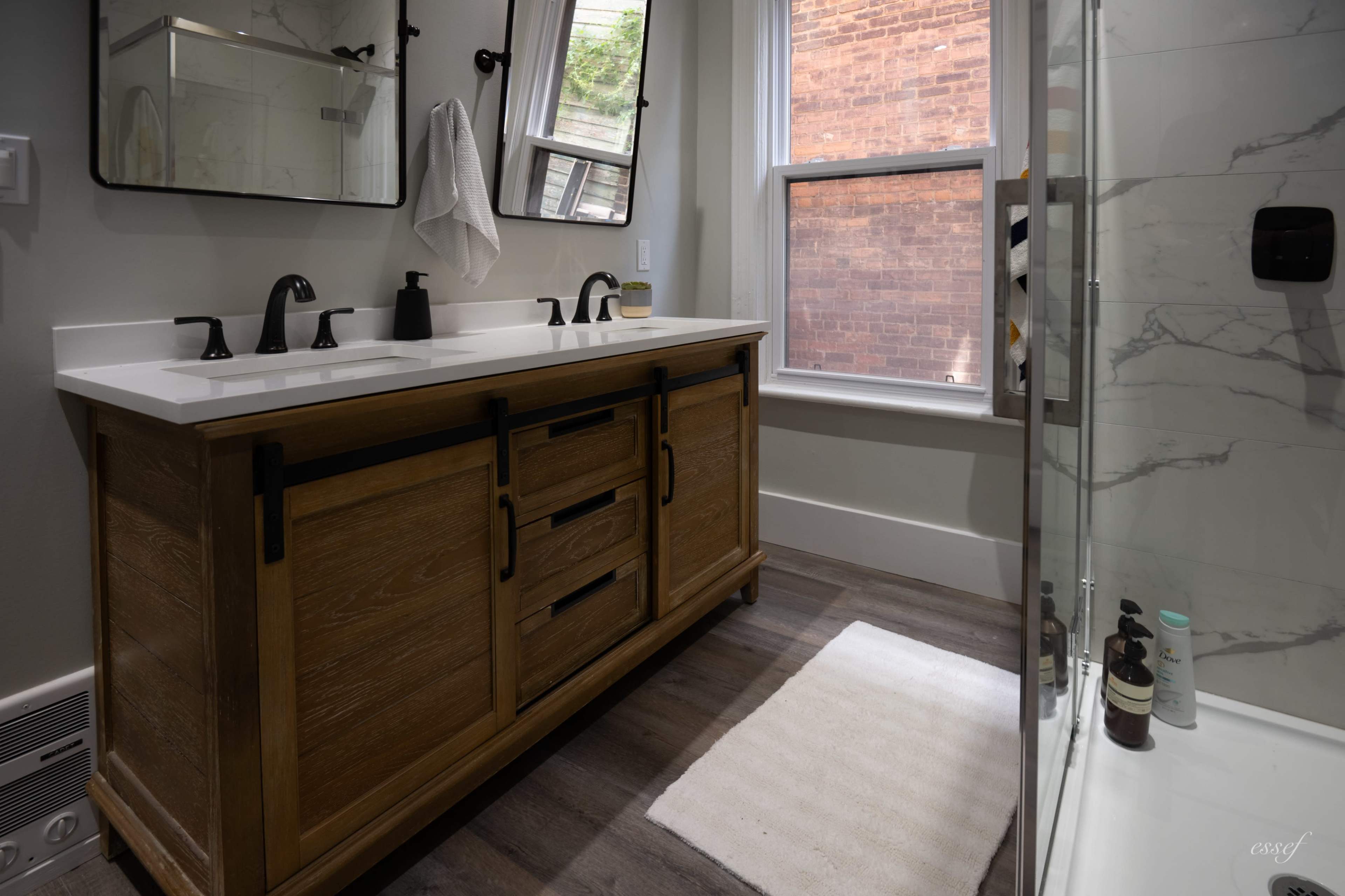 The image shows a modern bathroom featuring a wooden vanity with multiple drawers, a countertop with a sink, and a glass shower enclosure.