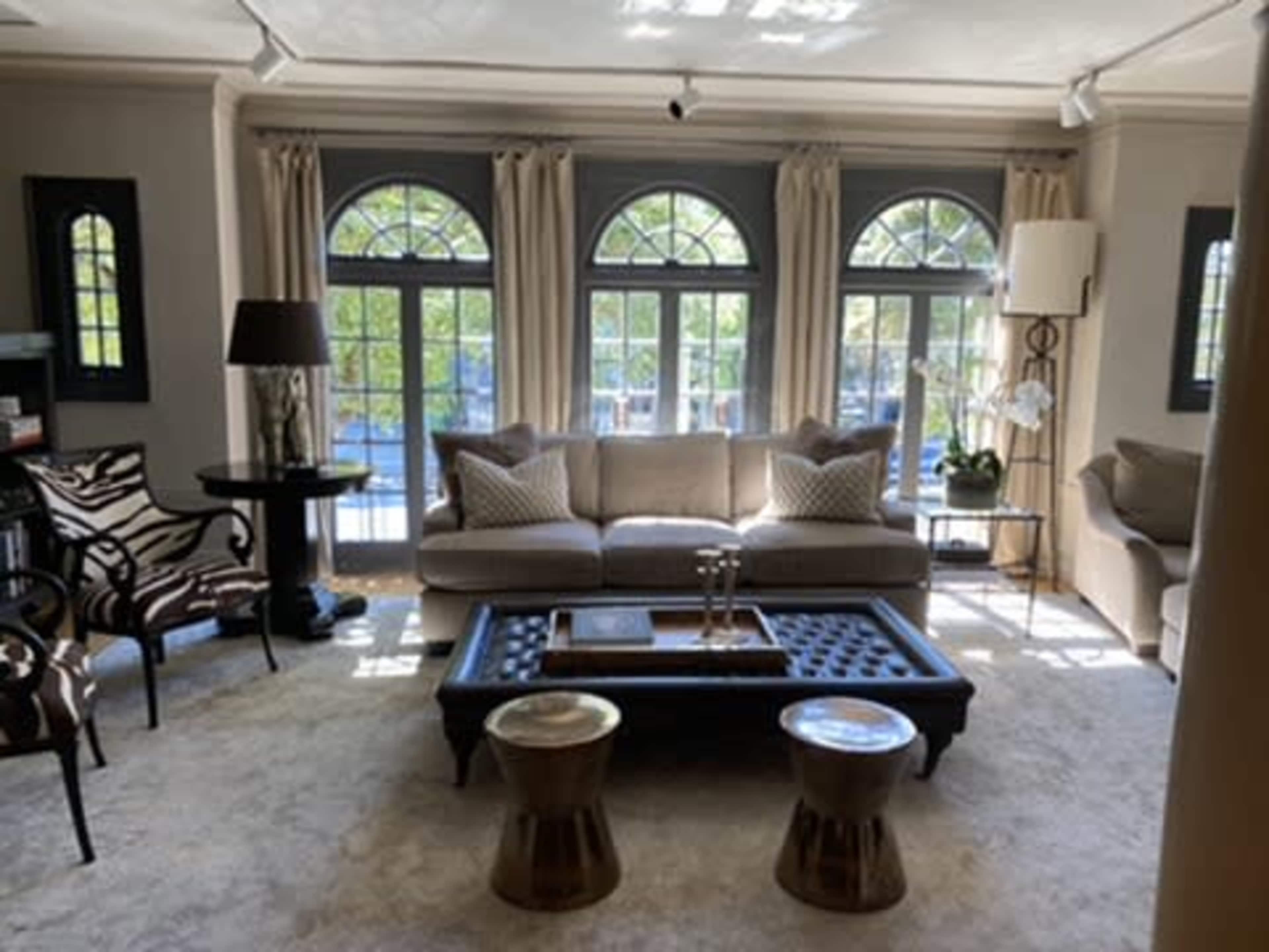 The living room features a light-colored sofa, two accent chairs, a coffee table, and large windows with arched tops that let in natural light.
