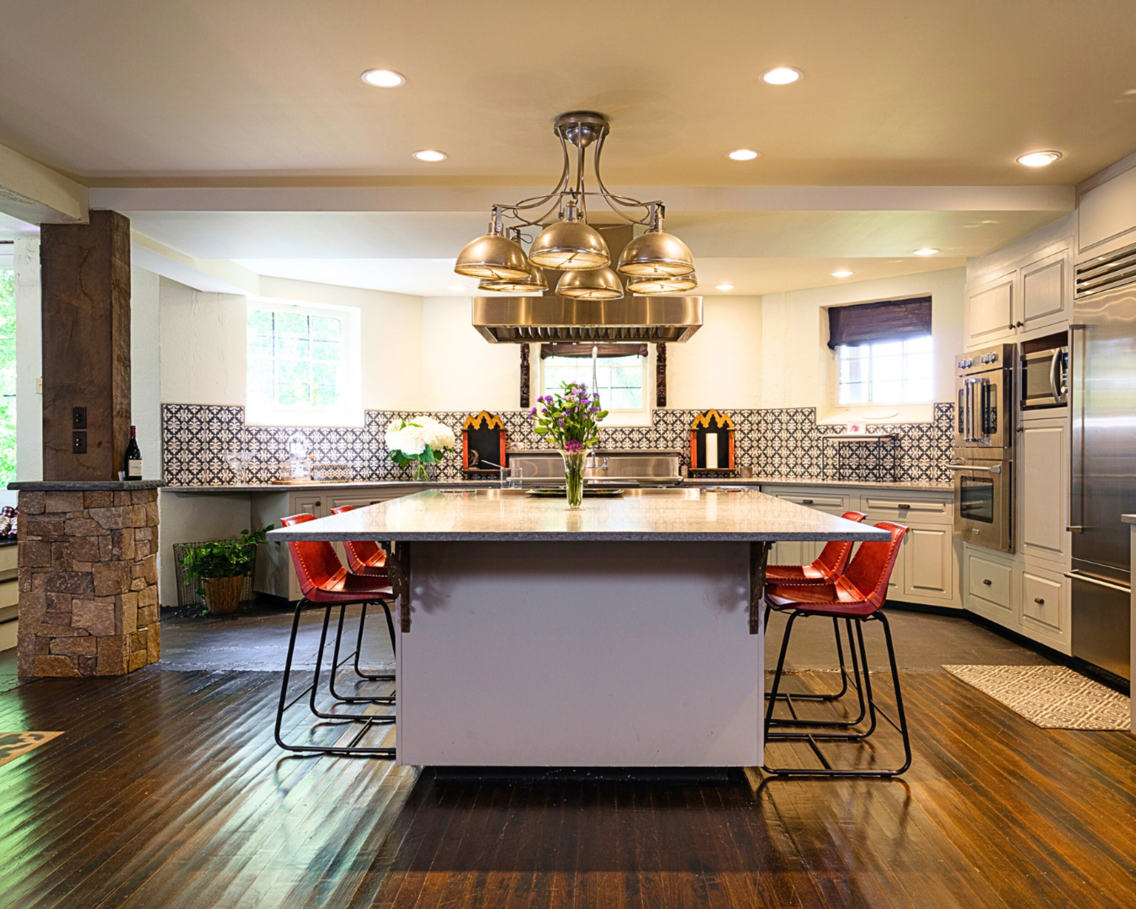 The image shows a modern kitchen with a large island, stainless steel appliances, and a decorative tile backsplash.