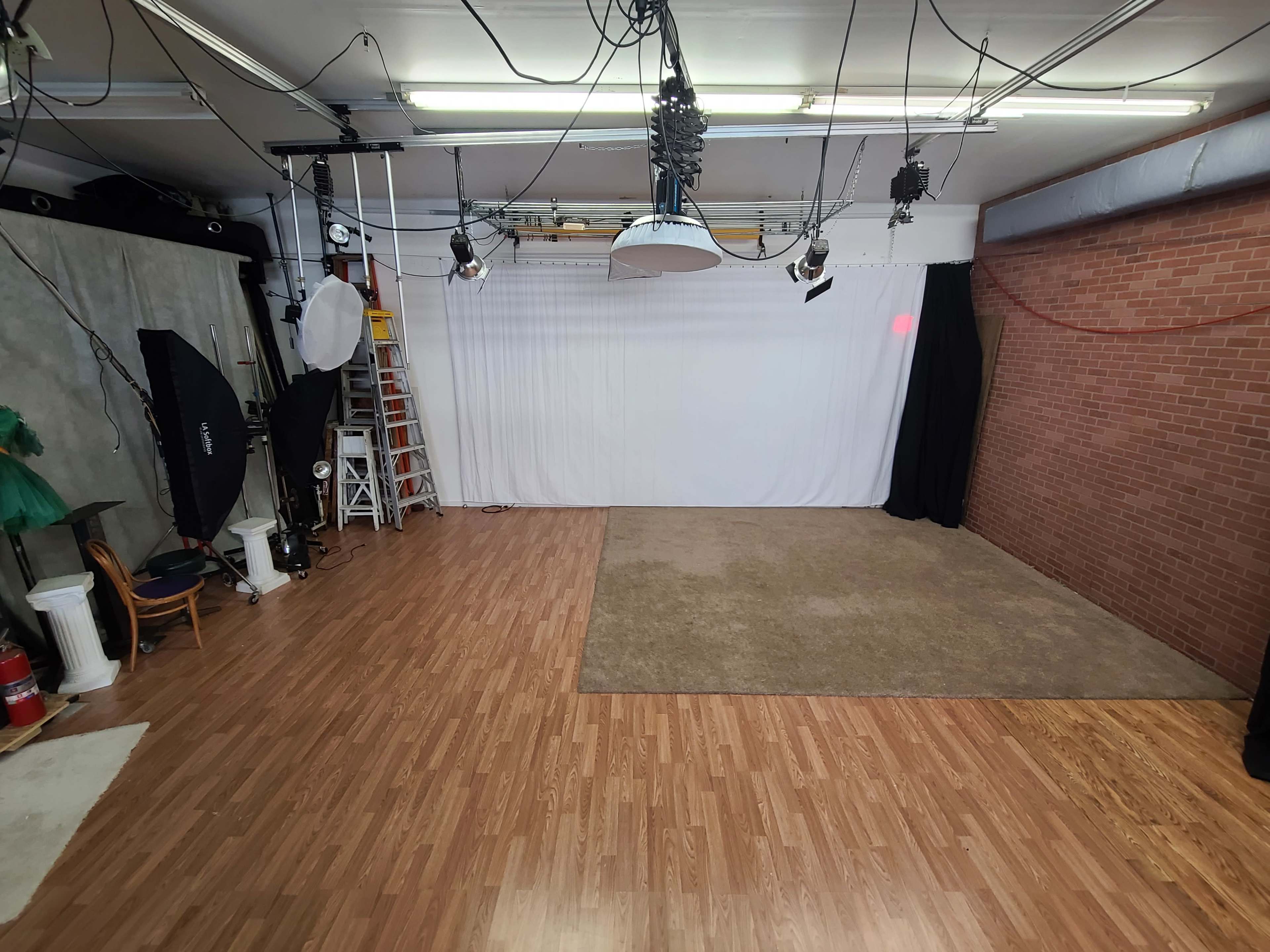 A spacious photography studio featuring a white backdrop, wooden flooring, and various lighting equipment.