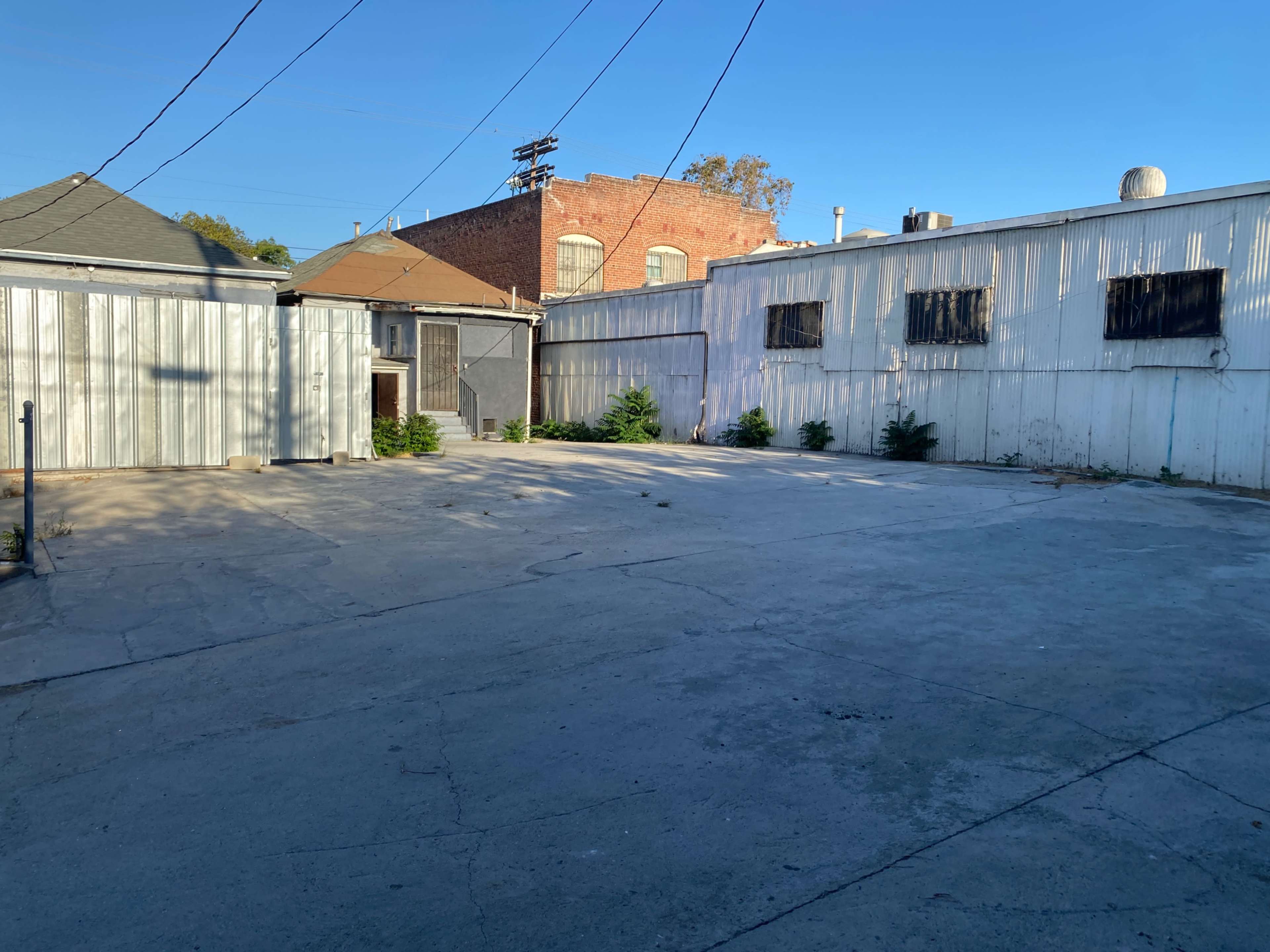 A vacant, concrete courtyard surrounded by industrial-style buildings under a clear blue sky.