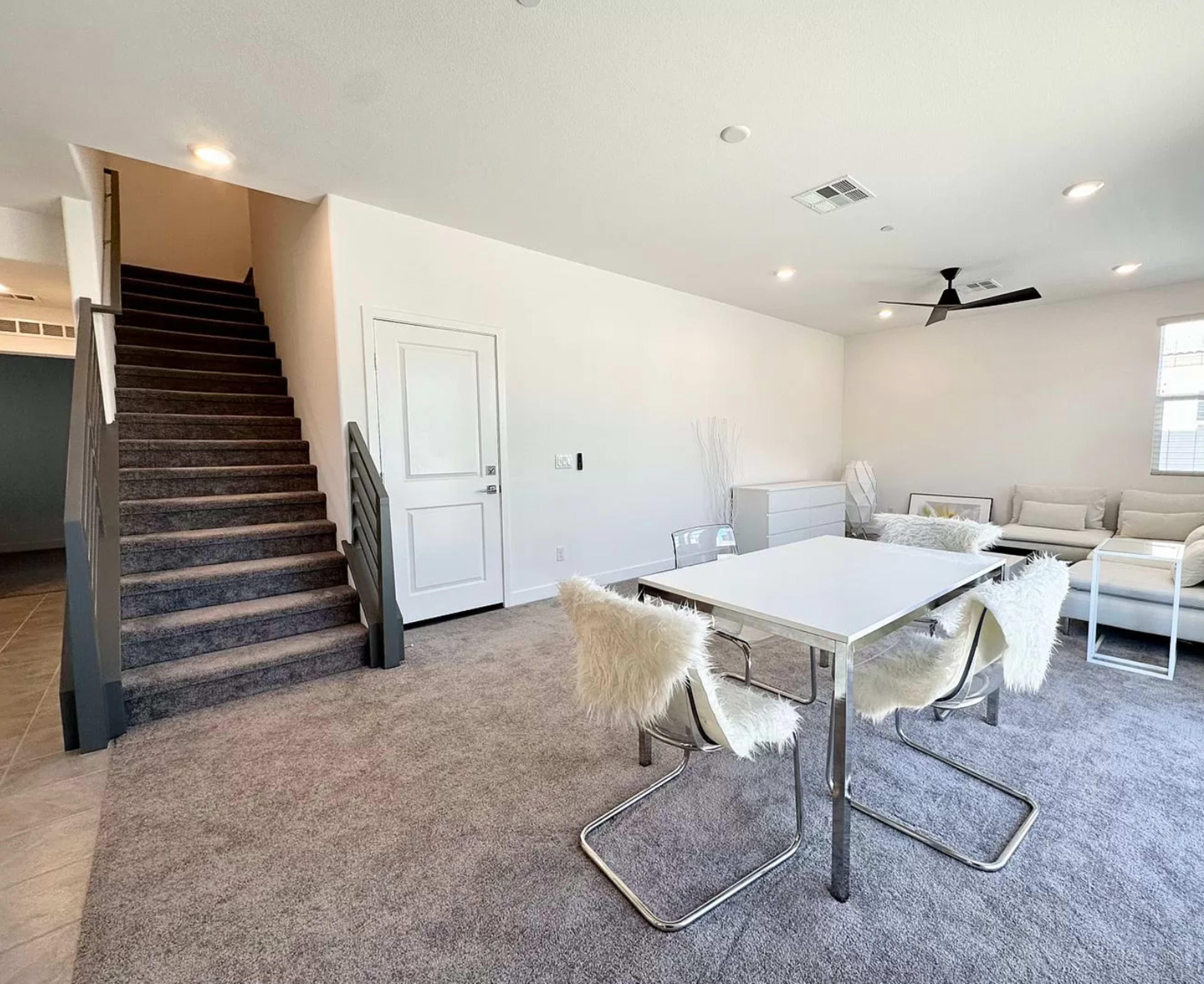 The spacious room features a dining table with chairs, a sofa area, and a staircase leading to the upper level.