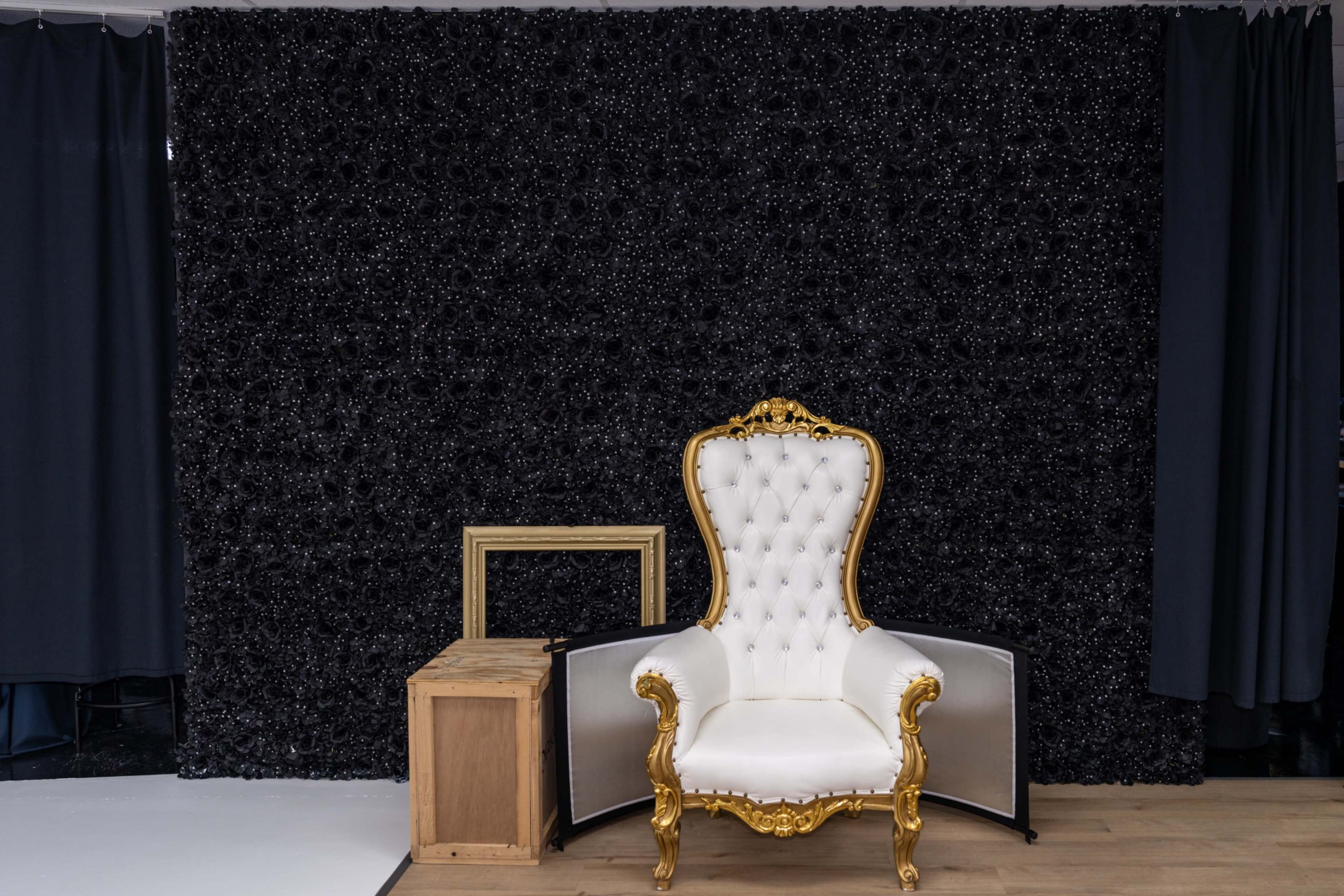 The image shows a luxurious white and gold chair beside a wooden box in front of a textured black backdrop.