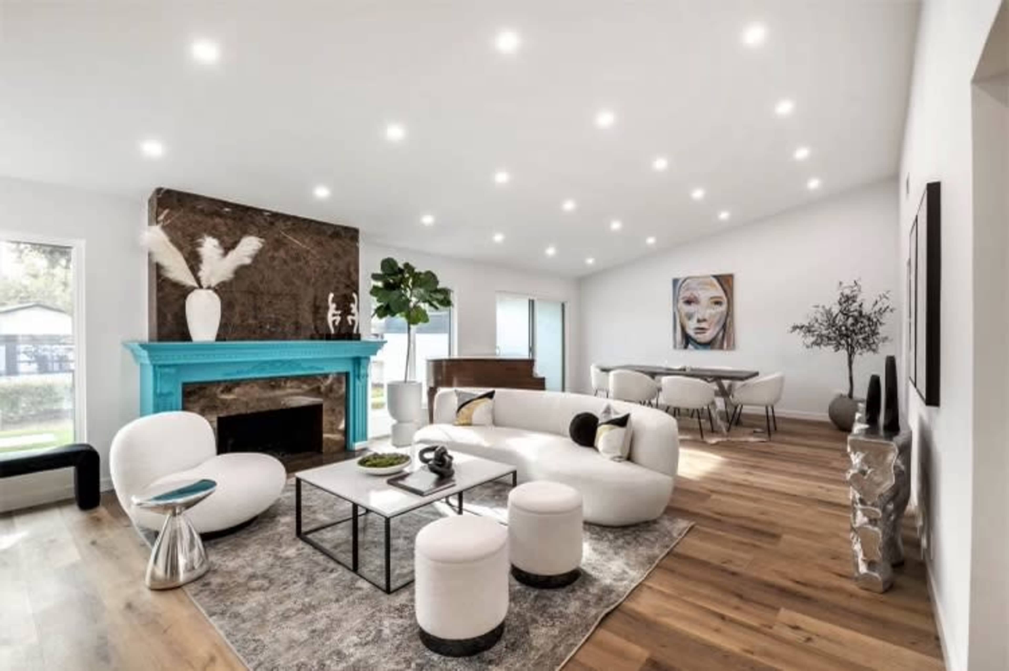 A modern living room features a turquoise fireplace, a round white sofa, and a sleek coffee table on a gray rug, complemented by large windows and minimalistic decor.