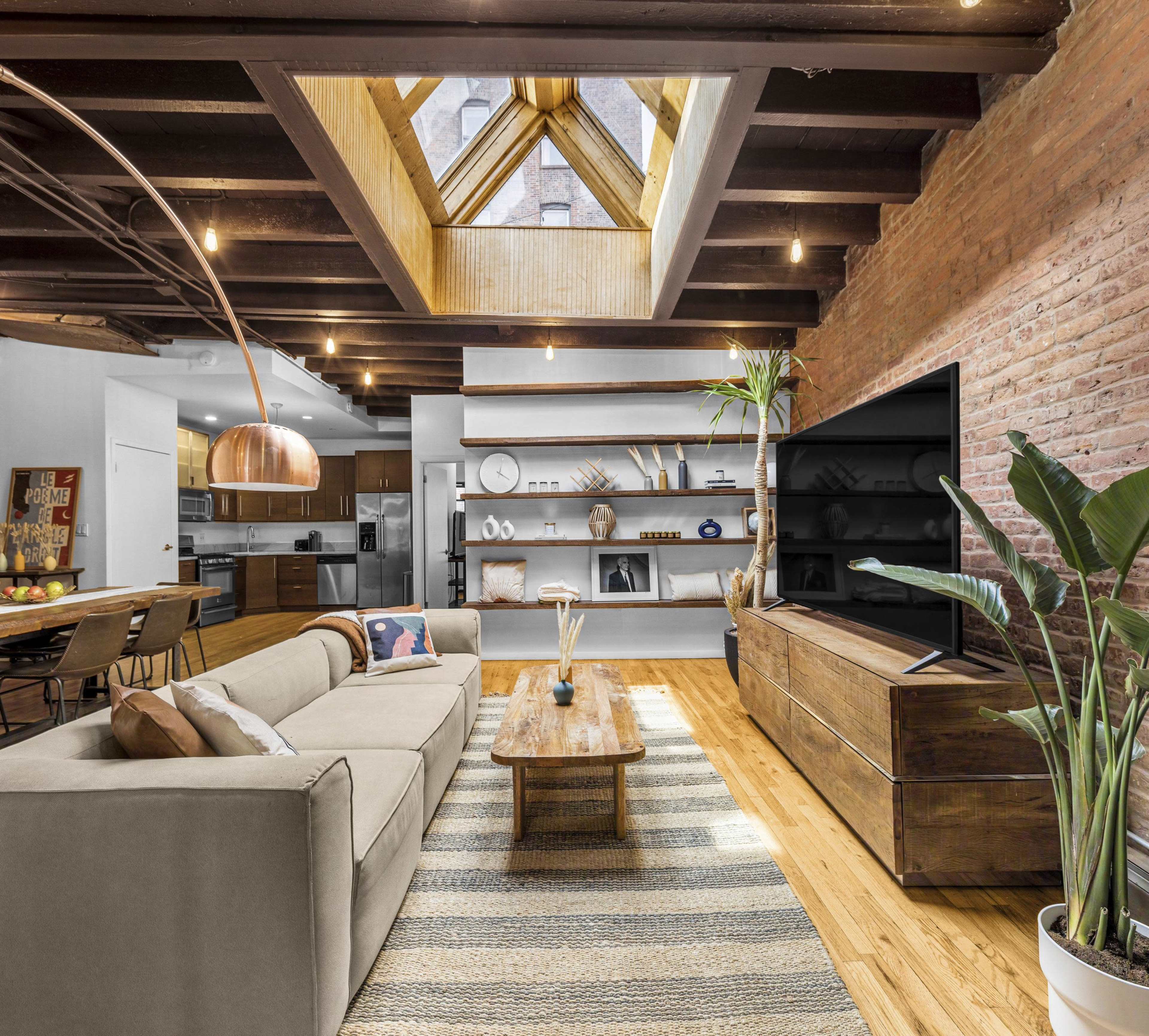 The living room features a cozy sectional sofa, a wooden coffee table, a large TV, and a skylight, with exposed beams and a mix of modern and rustic decor.