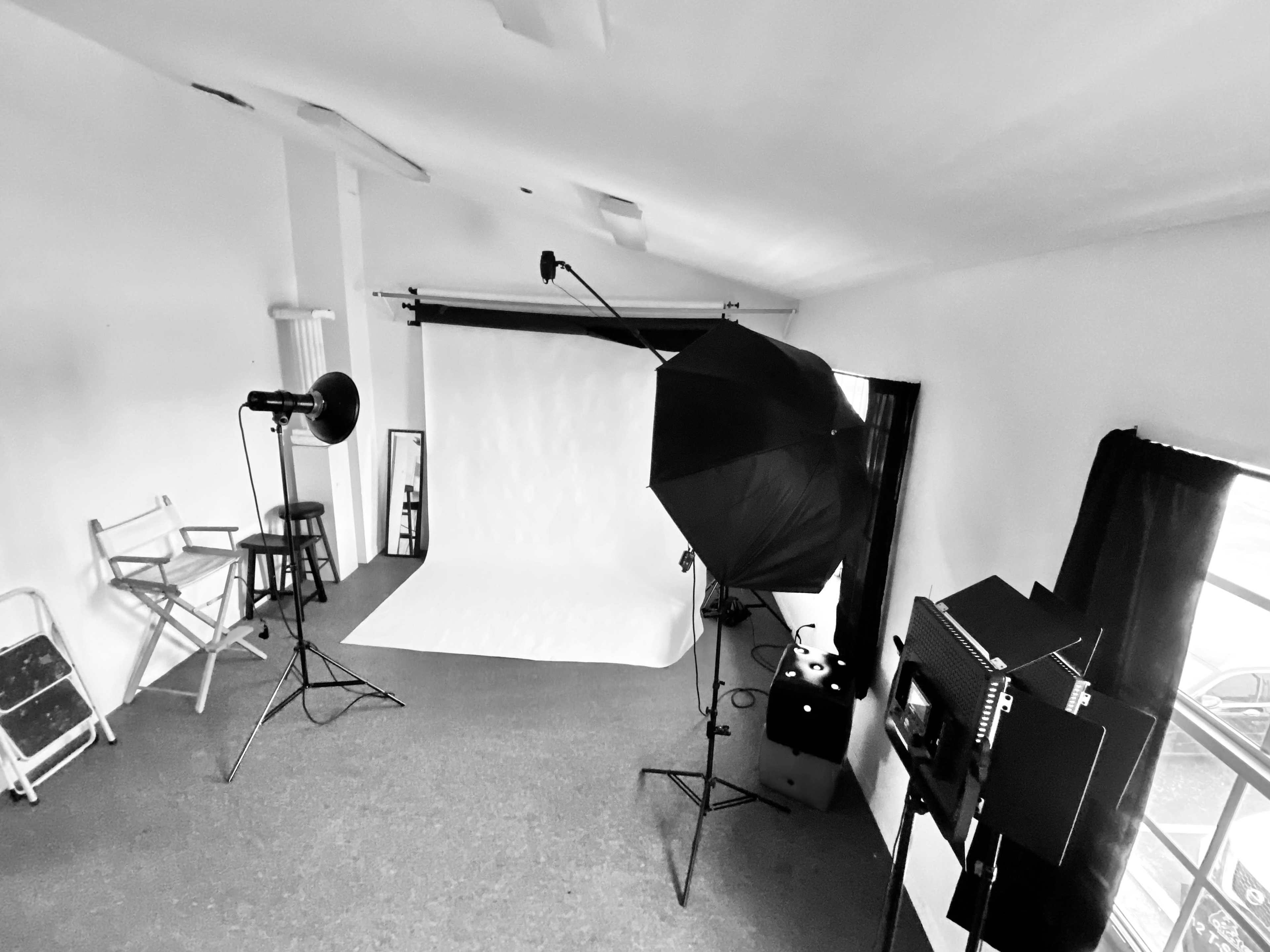 The image shows a photography studio featuring a blank backdrop, lighting equipment, and a director's chair.