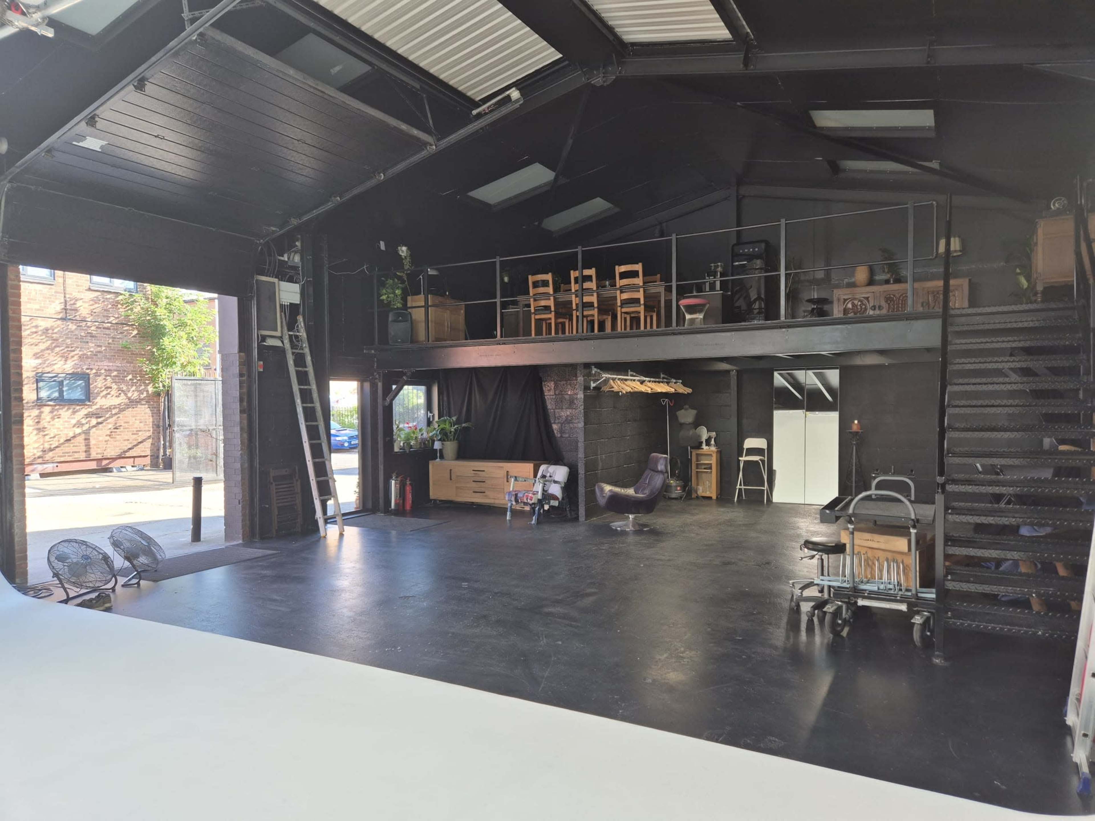 The image shows a spacious, industrial-style interior with a split-level design, featuring an open area with black flooring and wooden furniture arranged neatly.