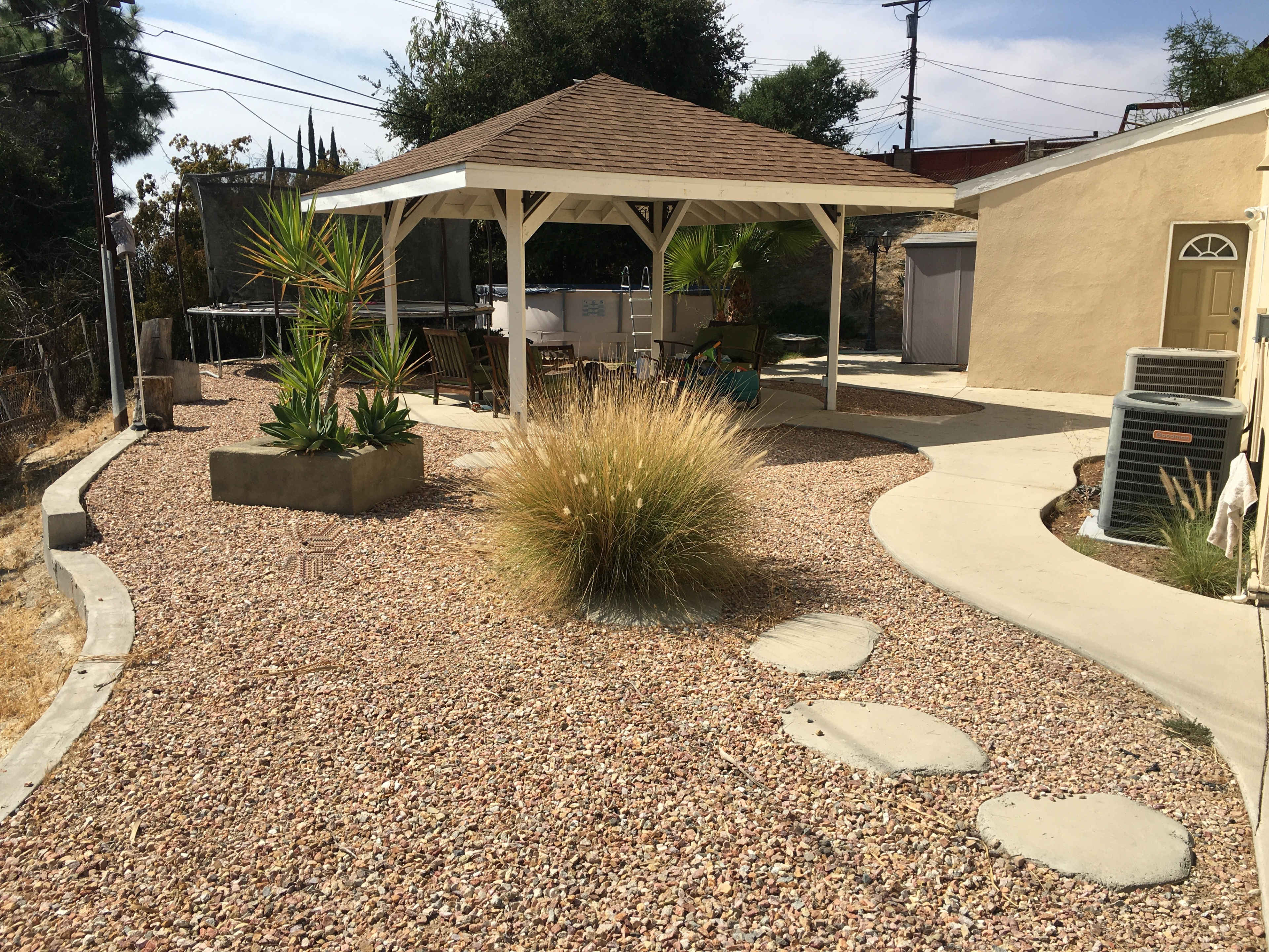 A gazebo with seating is surrounded by gravel and landscaping features in a residential backyard.