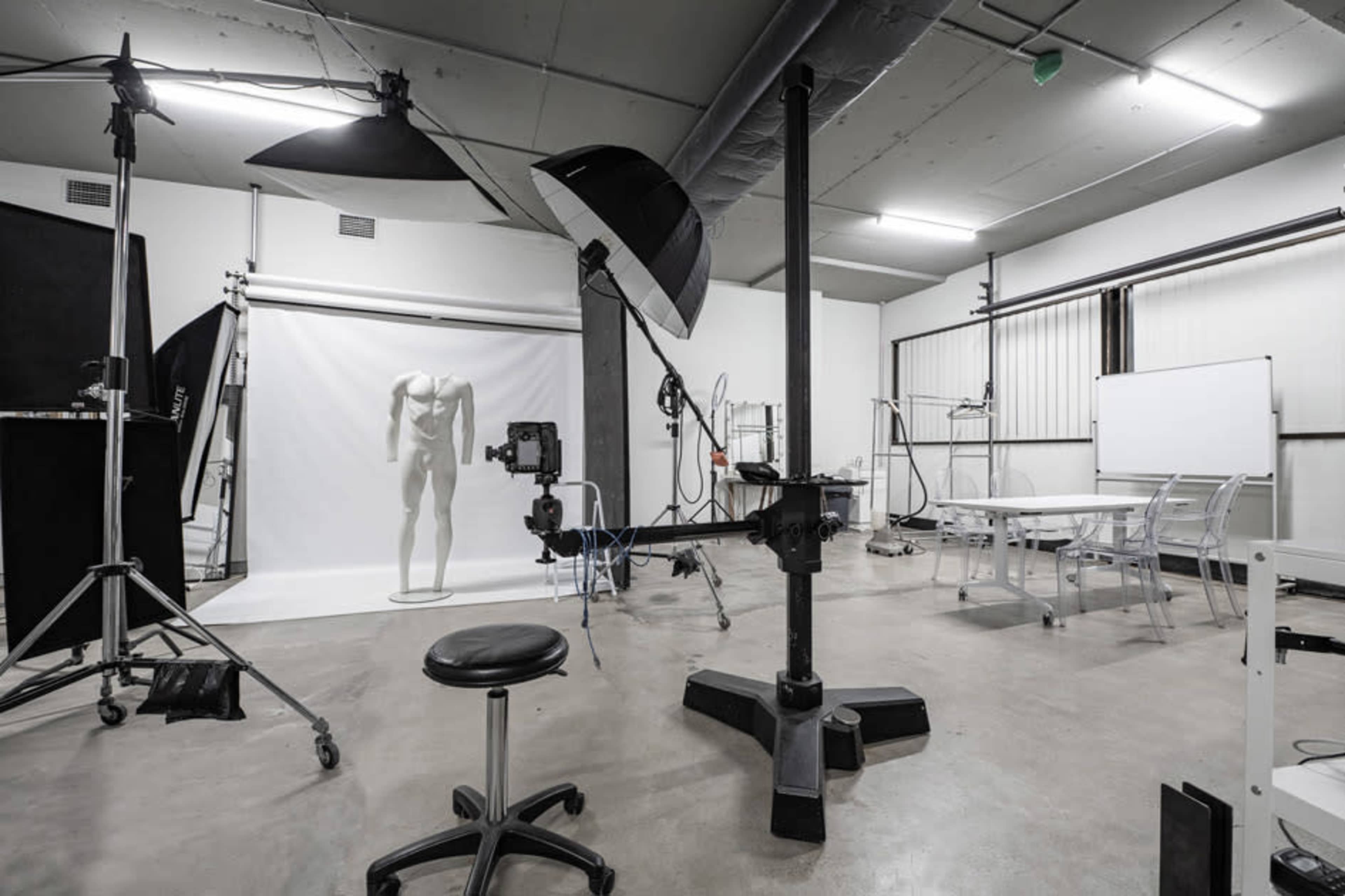 A photography studio with a blank backdrop, a mannequin, lighting equipment, and a round stool.
