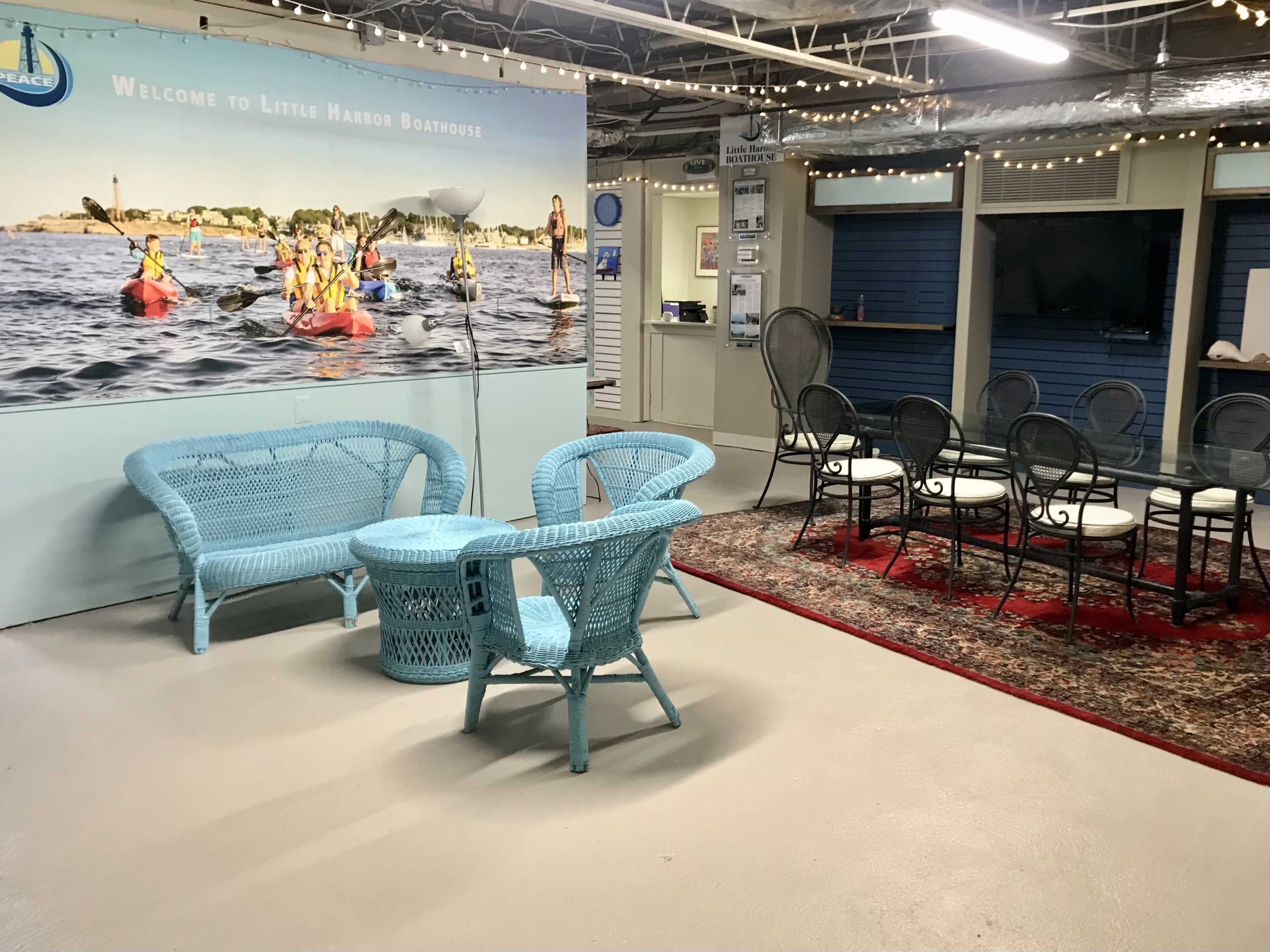 The image shows a recreational space with blue wicker furniture and a backdrop featuring a kayaking scene.