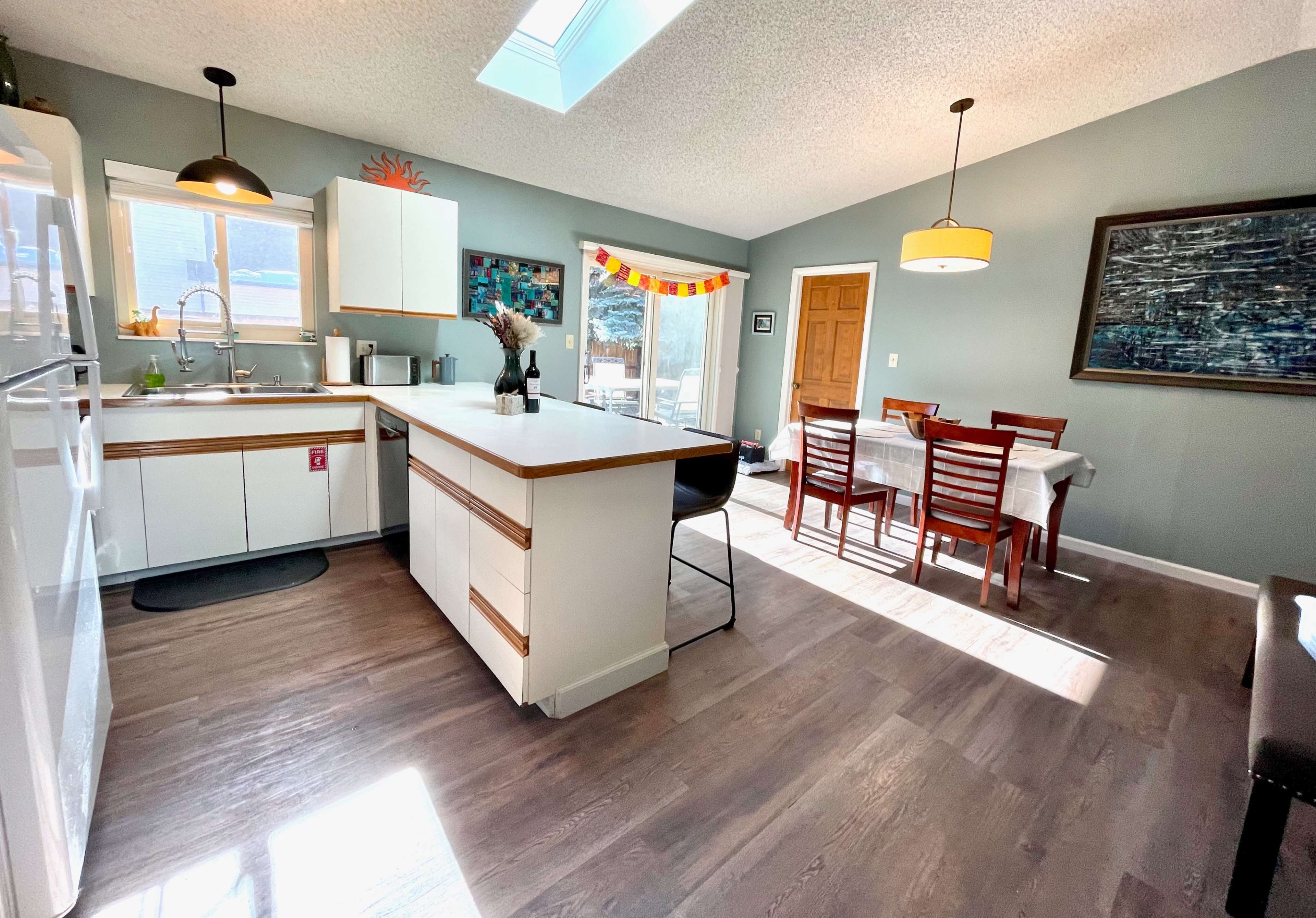 A modern kitchen and dining area features a skylight, wooden dining table, and sliding glass doors leading to an outdoor space.