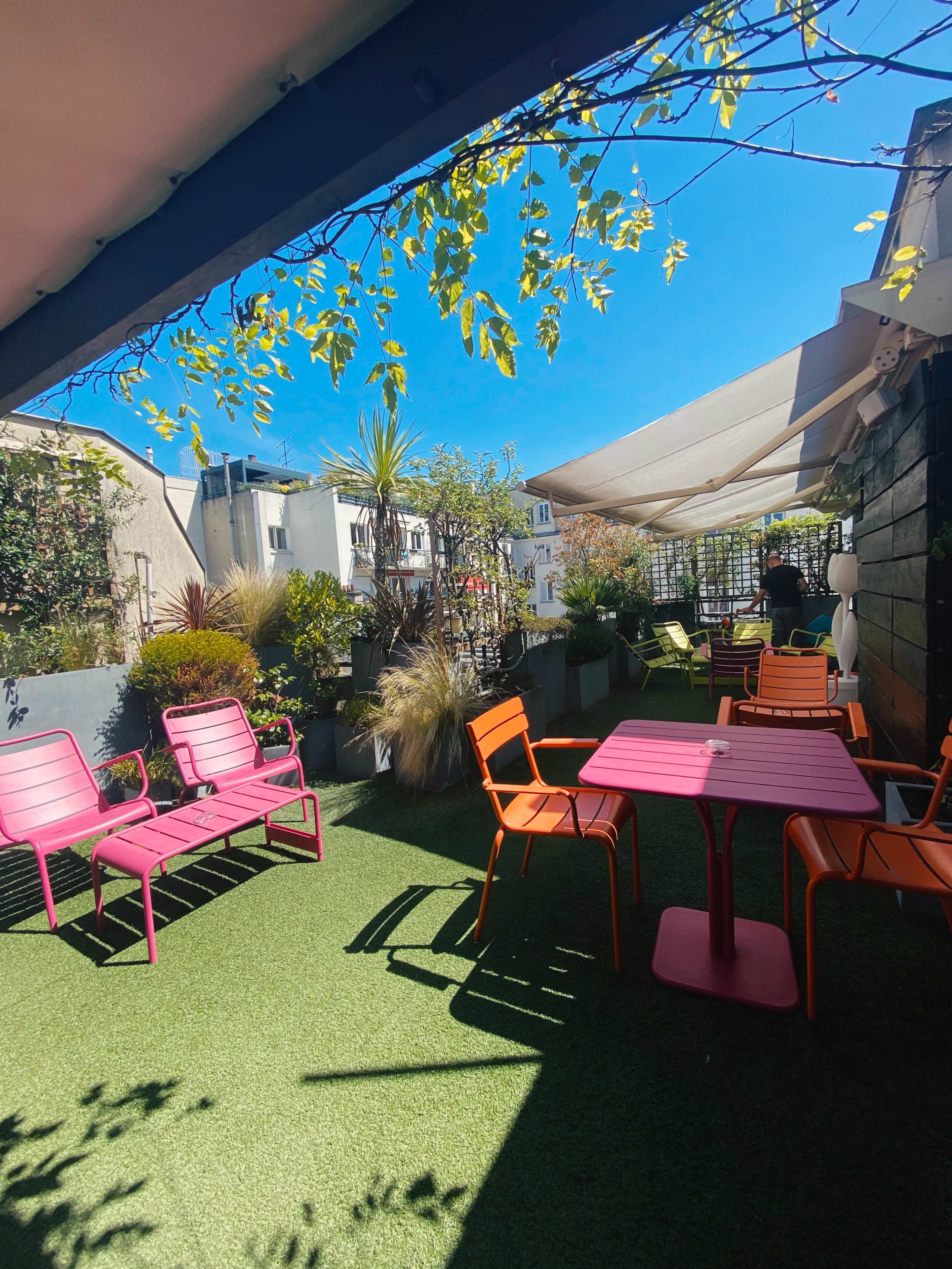 A rooftop terrace with colorful seating, artificial grass, and potted plants under a clear blue sky.
