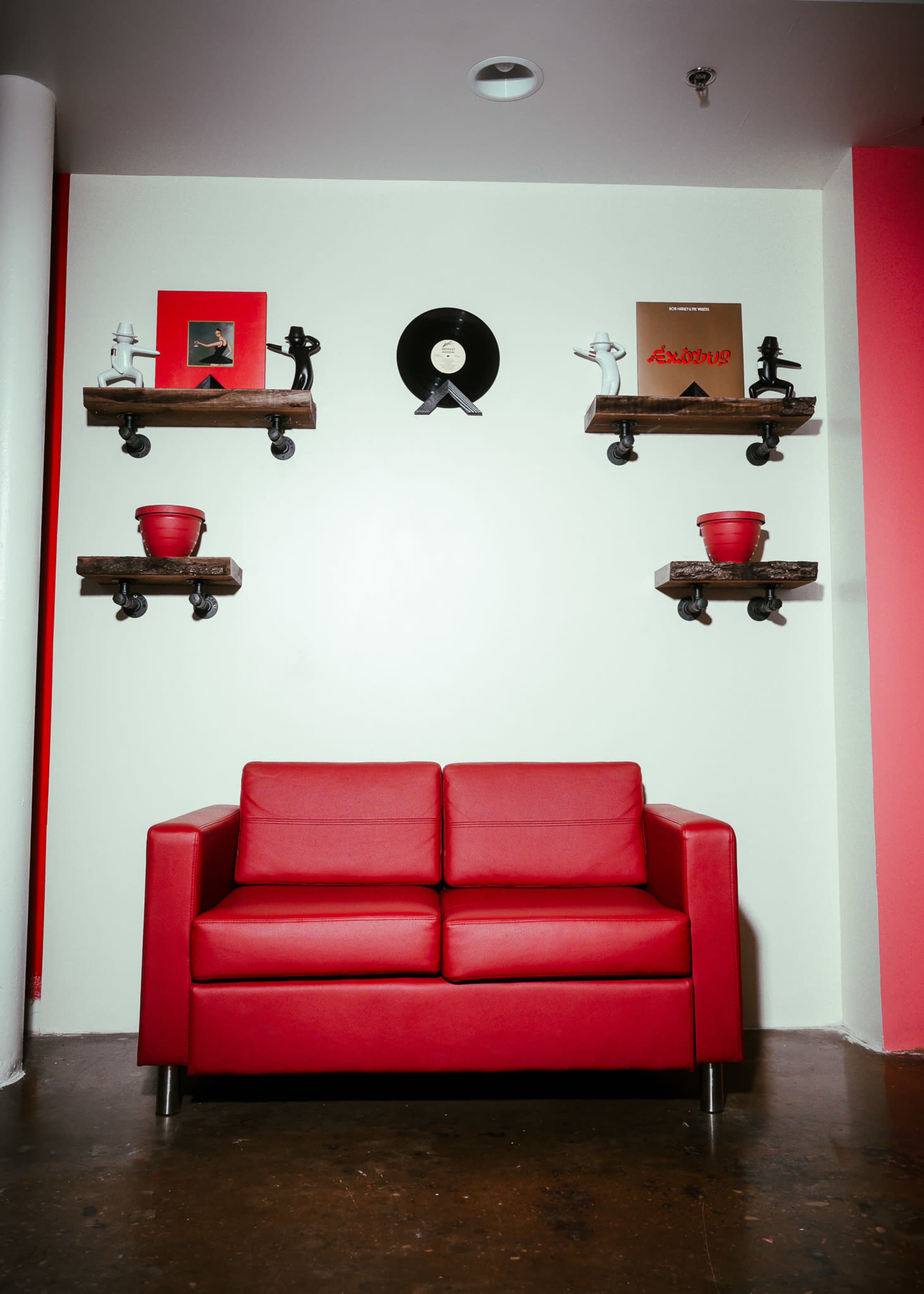 A red couch is positioned against a white wall, decorated with wooden shelves holding vinyl records and small potted plants.