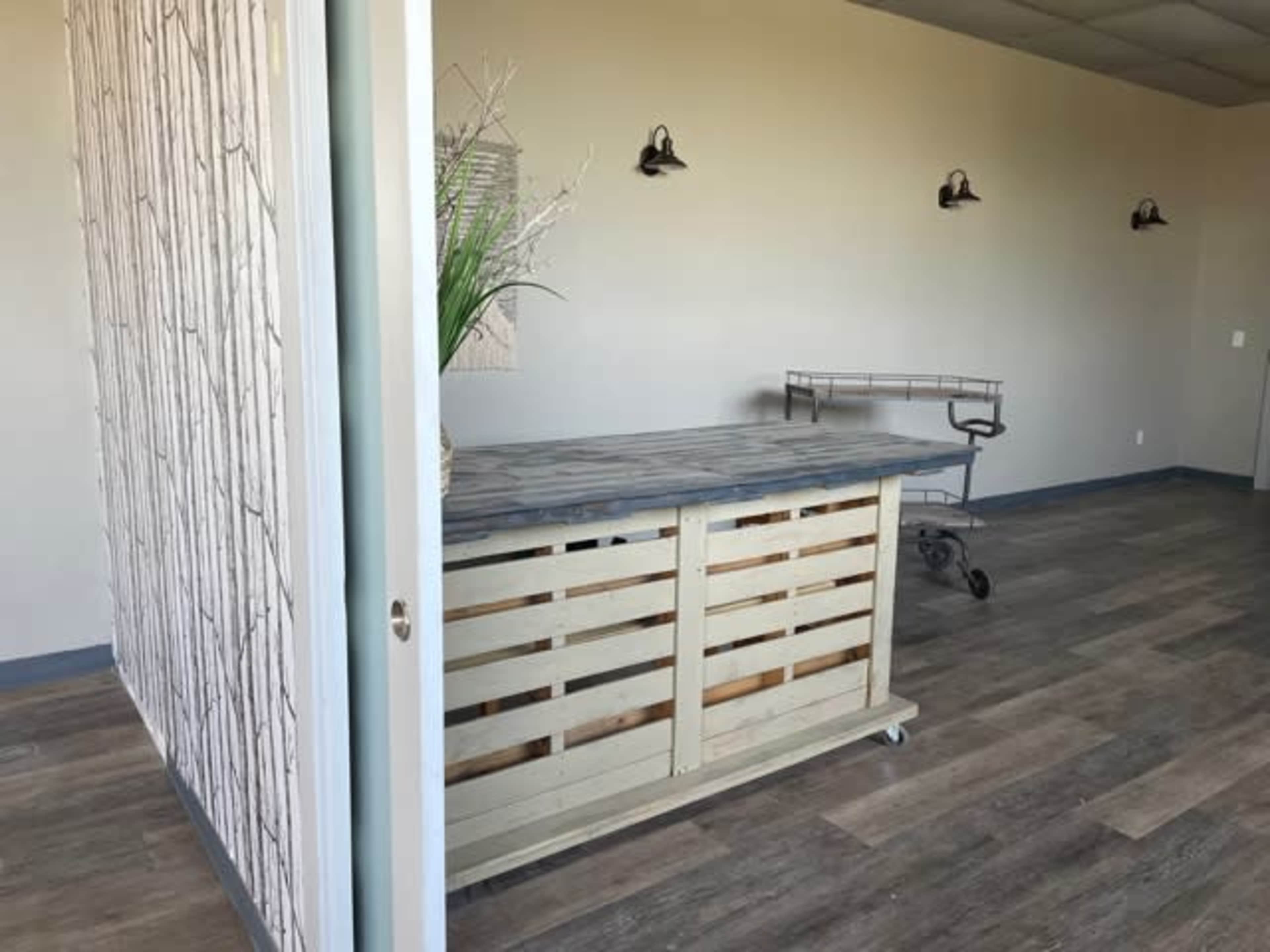 A sparsely furnished room with a wooden reception desk, a metal cart, and simple wall decor.