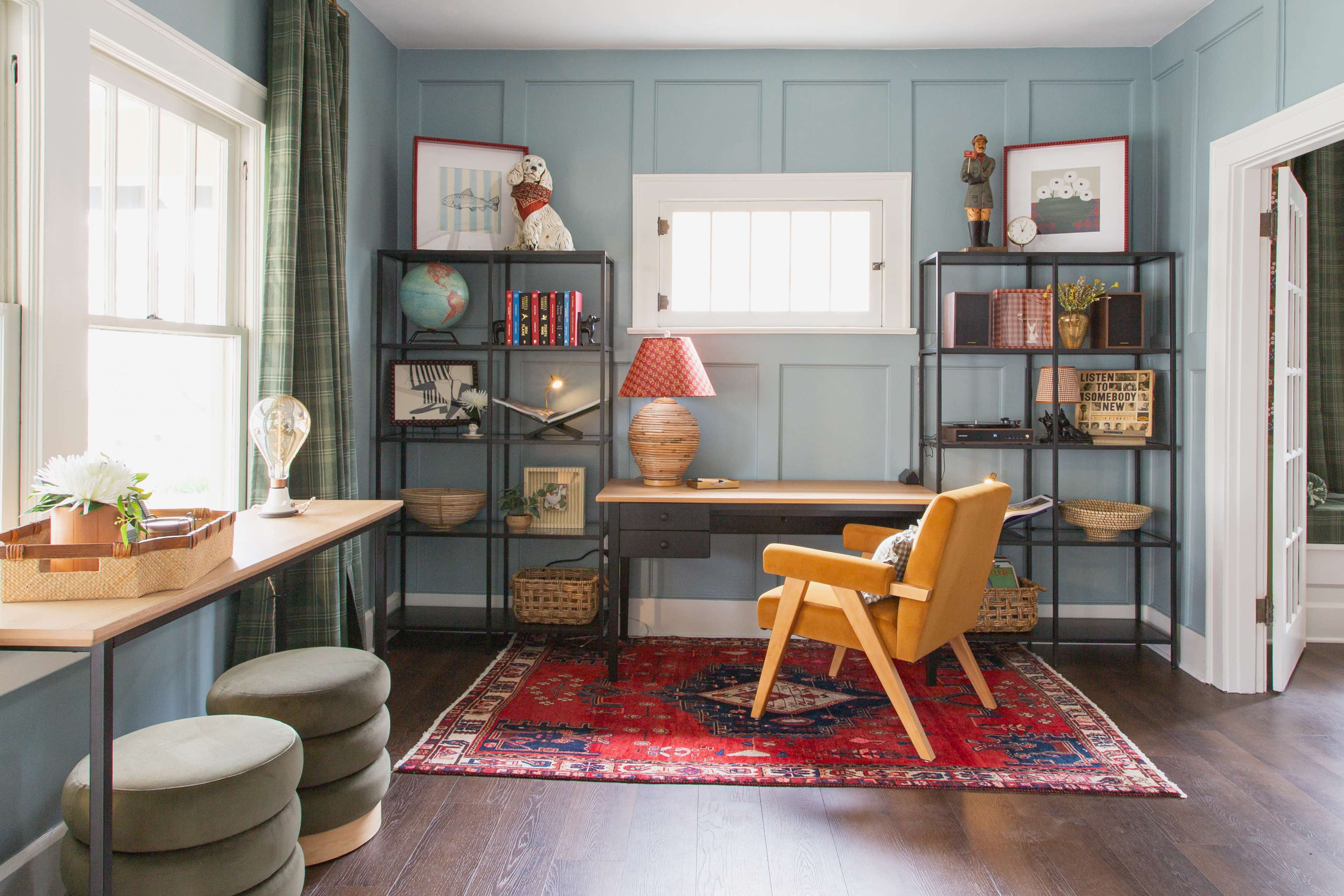 The image depicts a cozy home office featuring a yellow chair at a desk, surrounded by shelves holding books, decorative items, and a lamp, with a patterned rug on the floor.