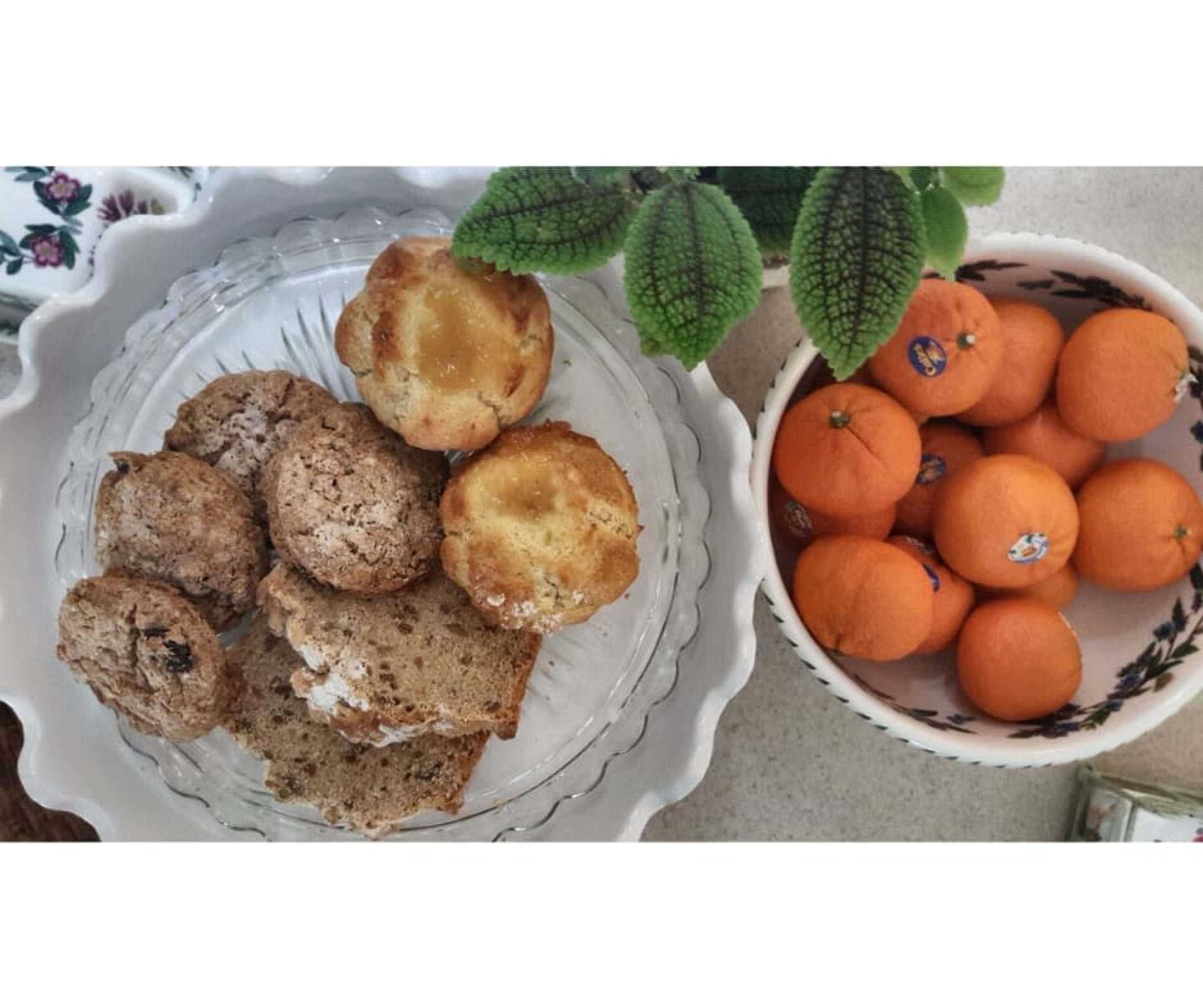 A plate of assorted baked goods including muffins and slices of bread, alongside a bowl of small oranges.