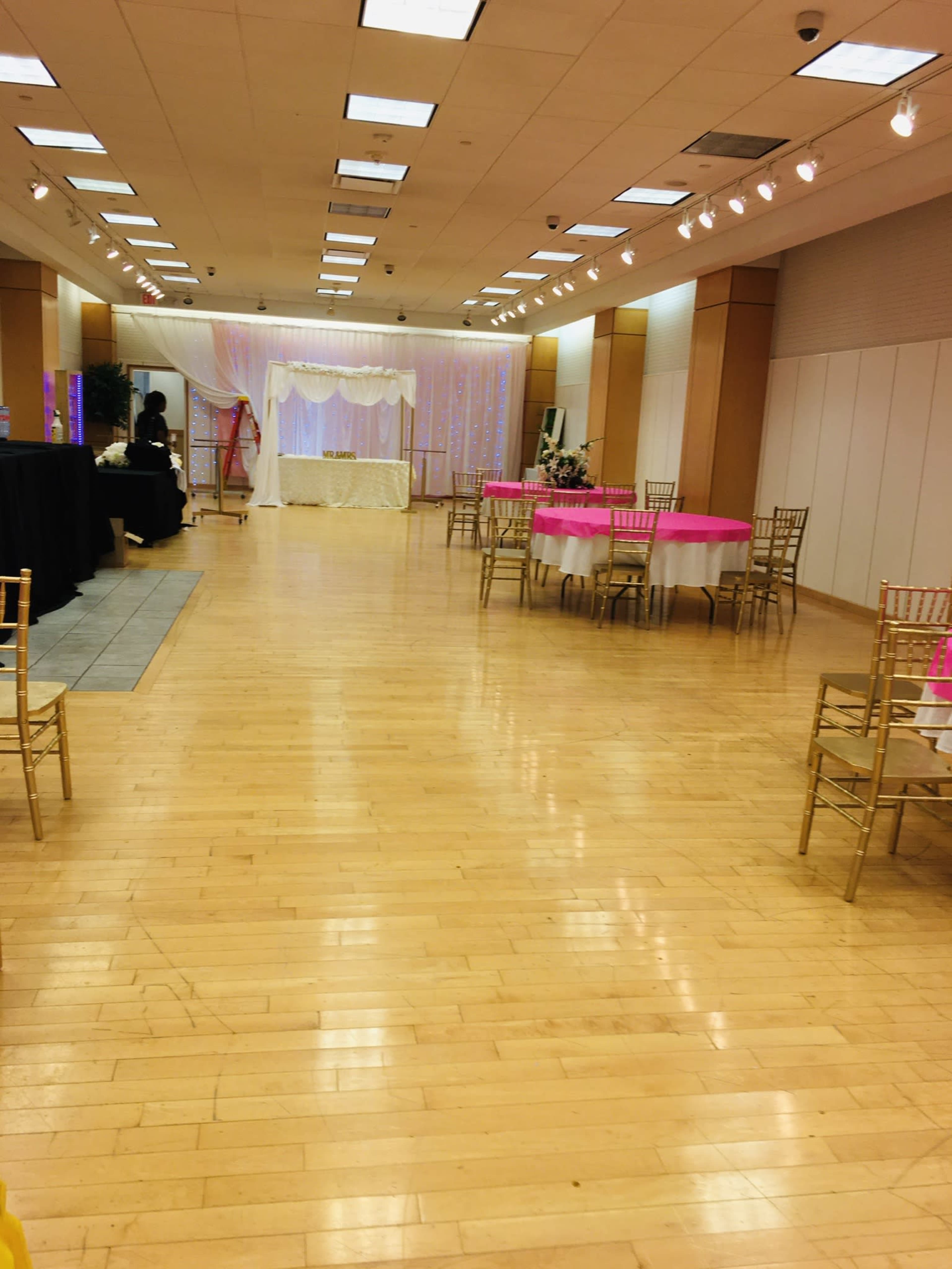 A spacious event hall with tables dressed in pink and gold chairs, set up for a celebration.