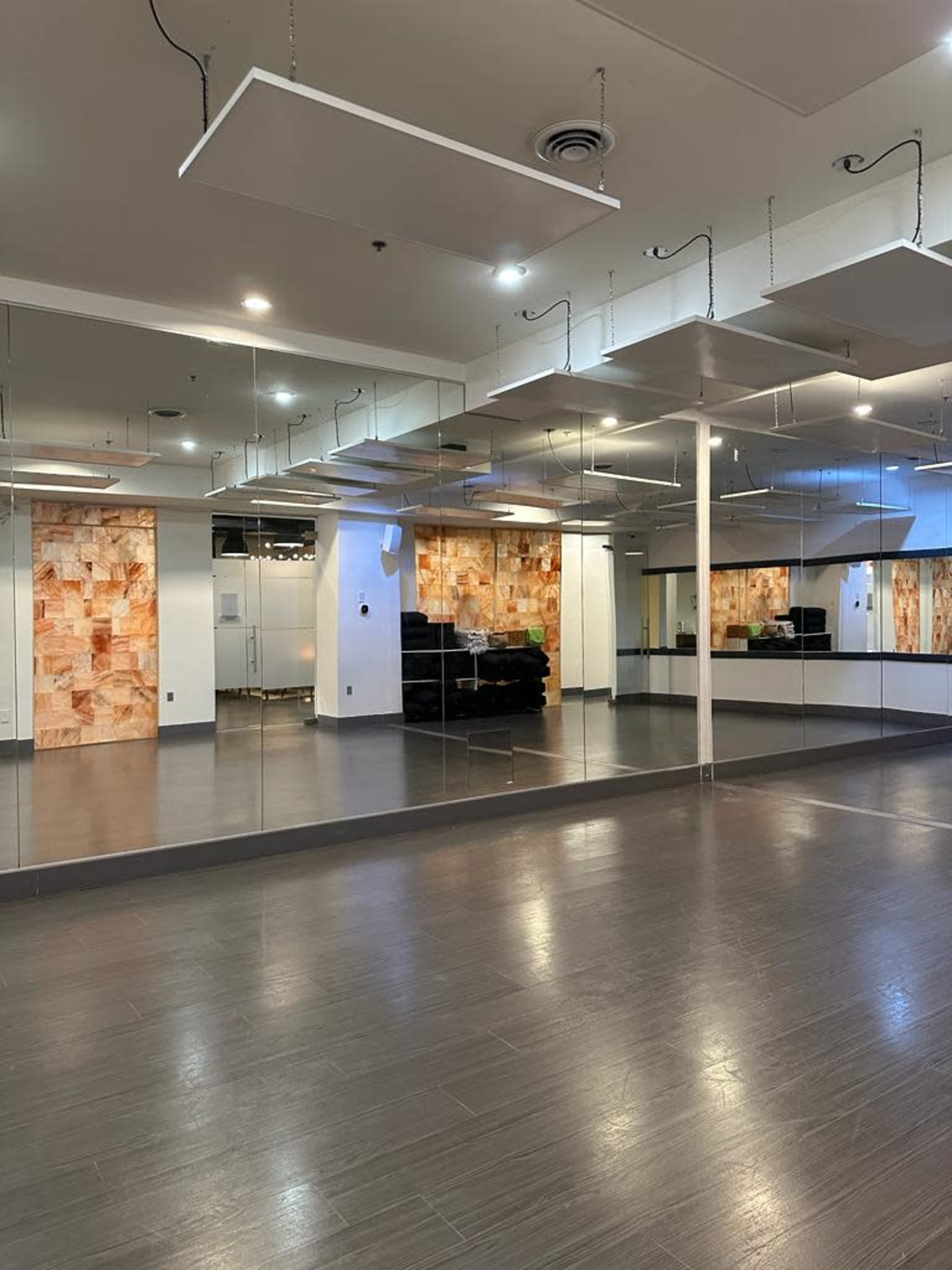 A spacious dance studio with mirrored walls and an industrial-style ceiling featuring suspended light fixtures.