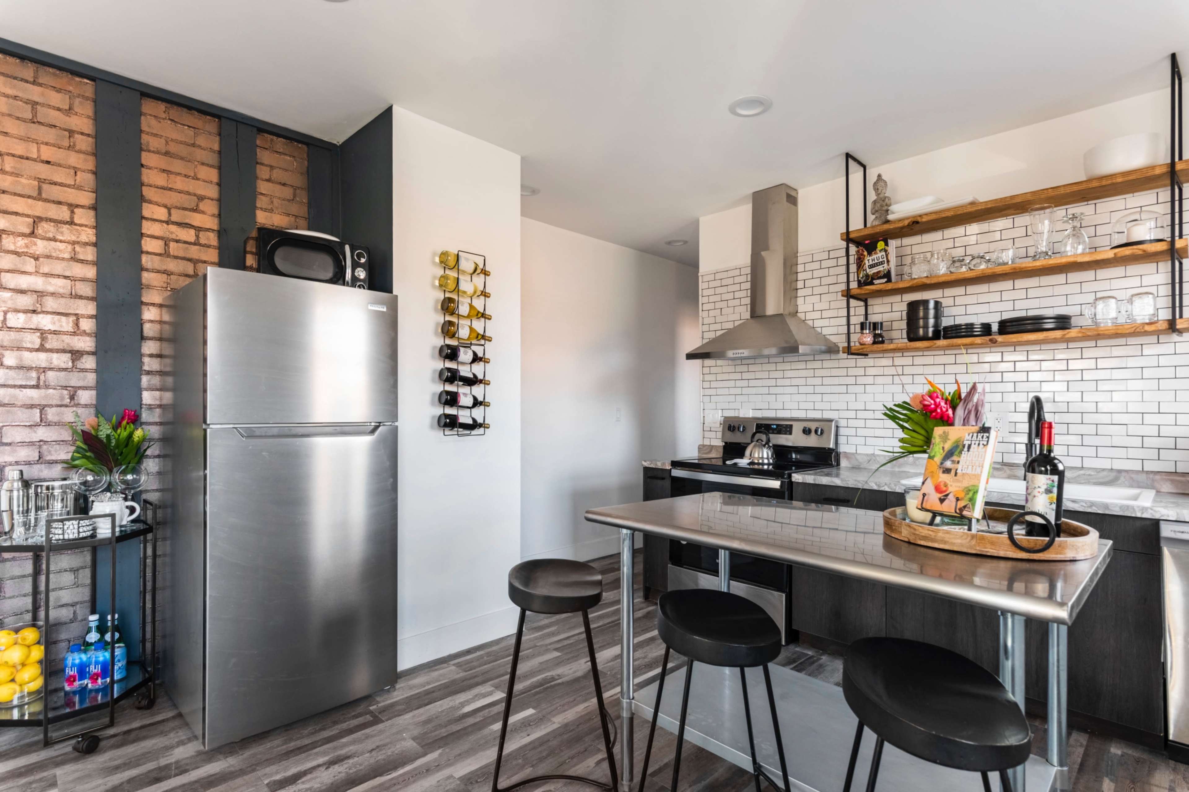 A modern kitchen with a stainless steel fridge, a wine rack on the wall, and a central island with bar stools.