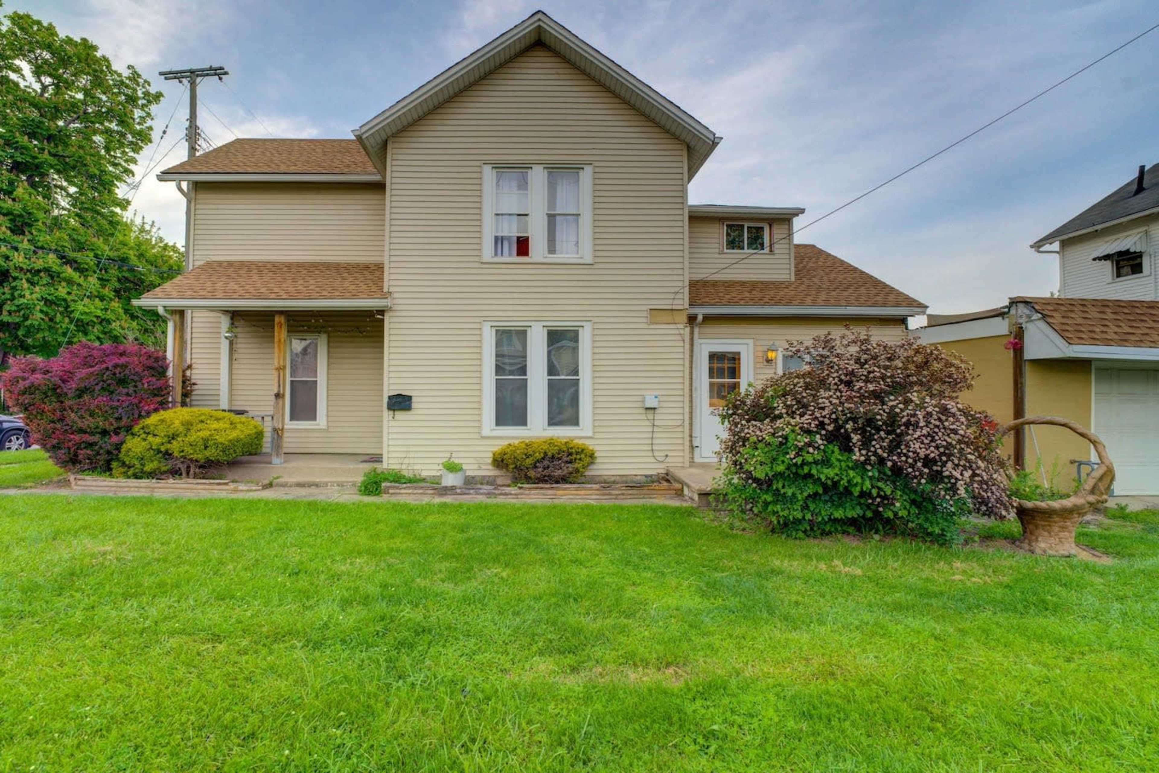 A two-story house with beige siding and a well-maintained front yard featuring bushes and grass.