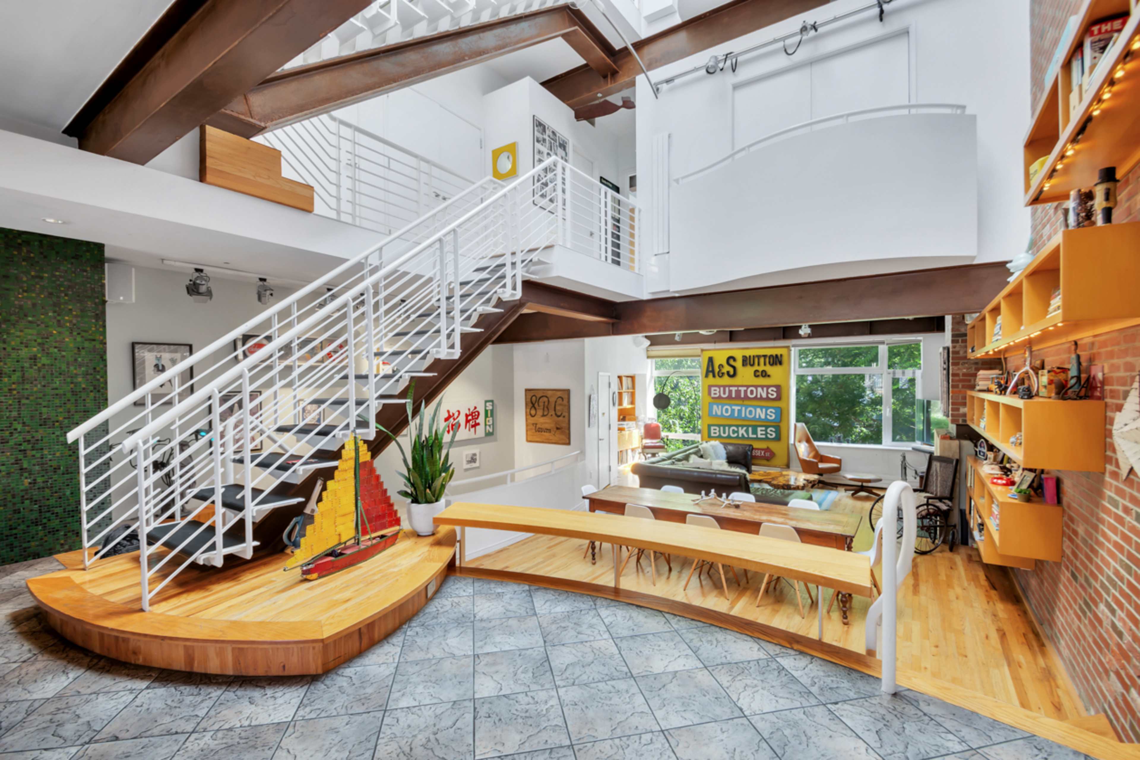 A modern open-concept home features a wooden staircase, a large dining area, and a mix of greenery and decor elements.