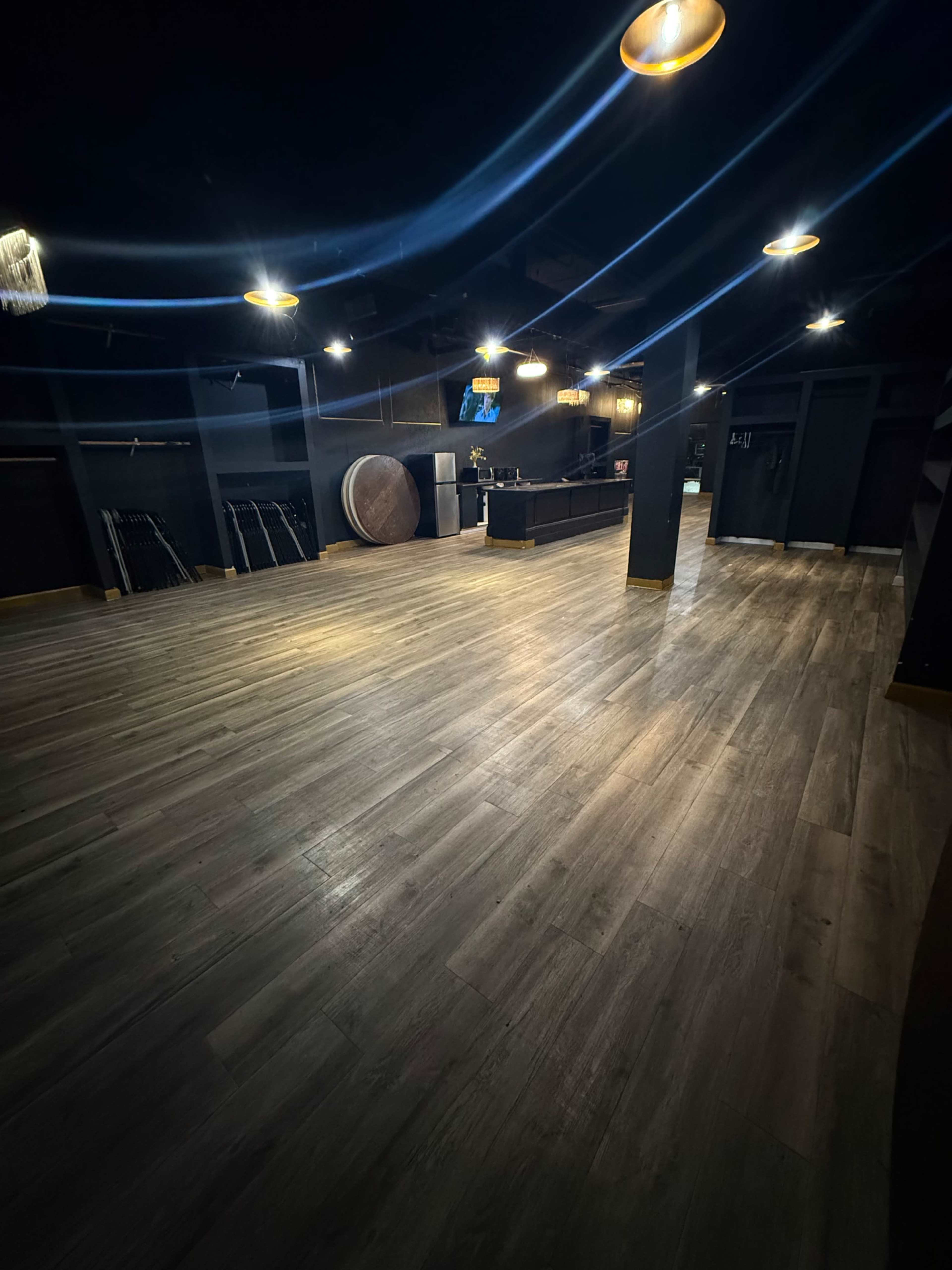 The image shows a dimly lit indoor space with a polished wooden floor, illuminated by overhead lights, and several empty shelves along the walls.