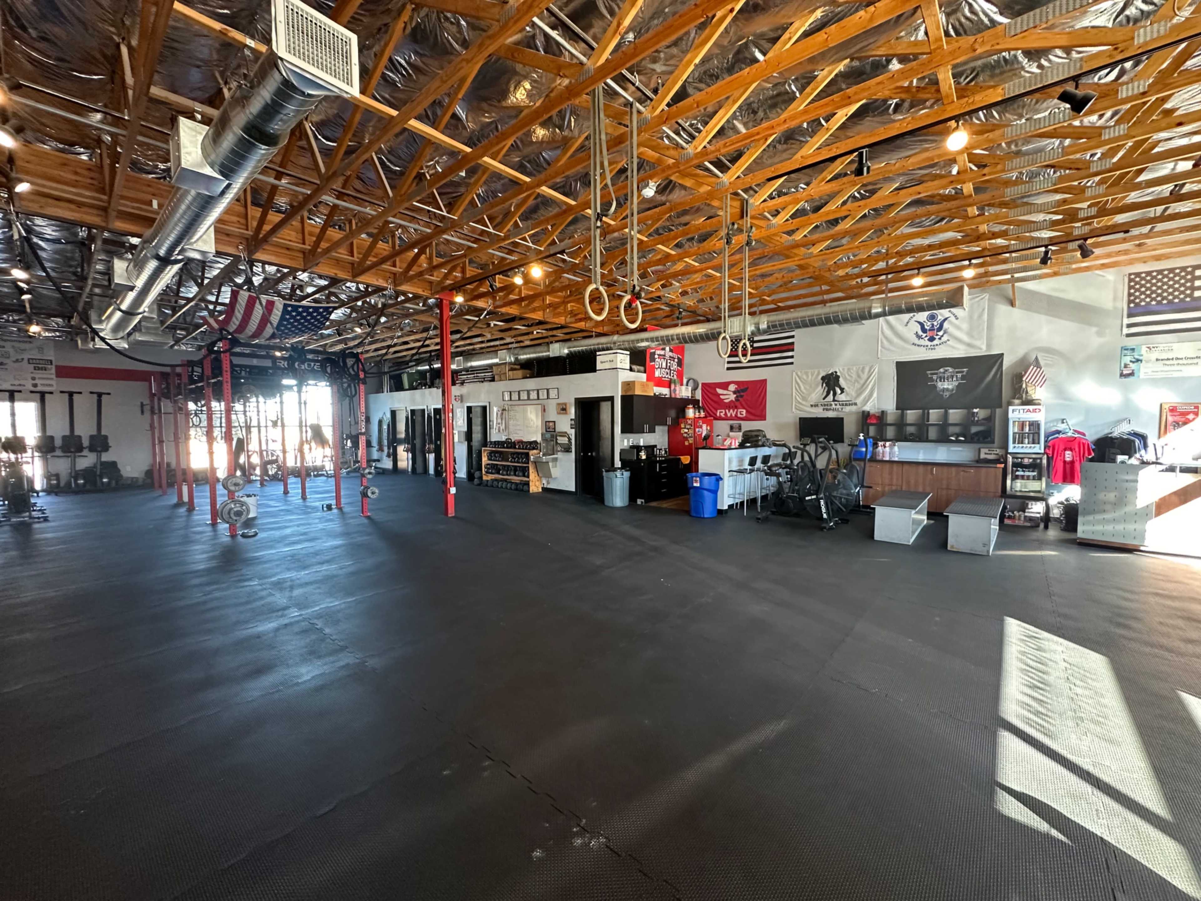 A spacious gym interior with exposed wooden beams, various exercise equipment, and patriotic decorations on the walls.