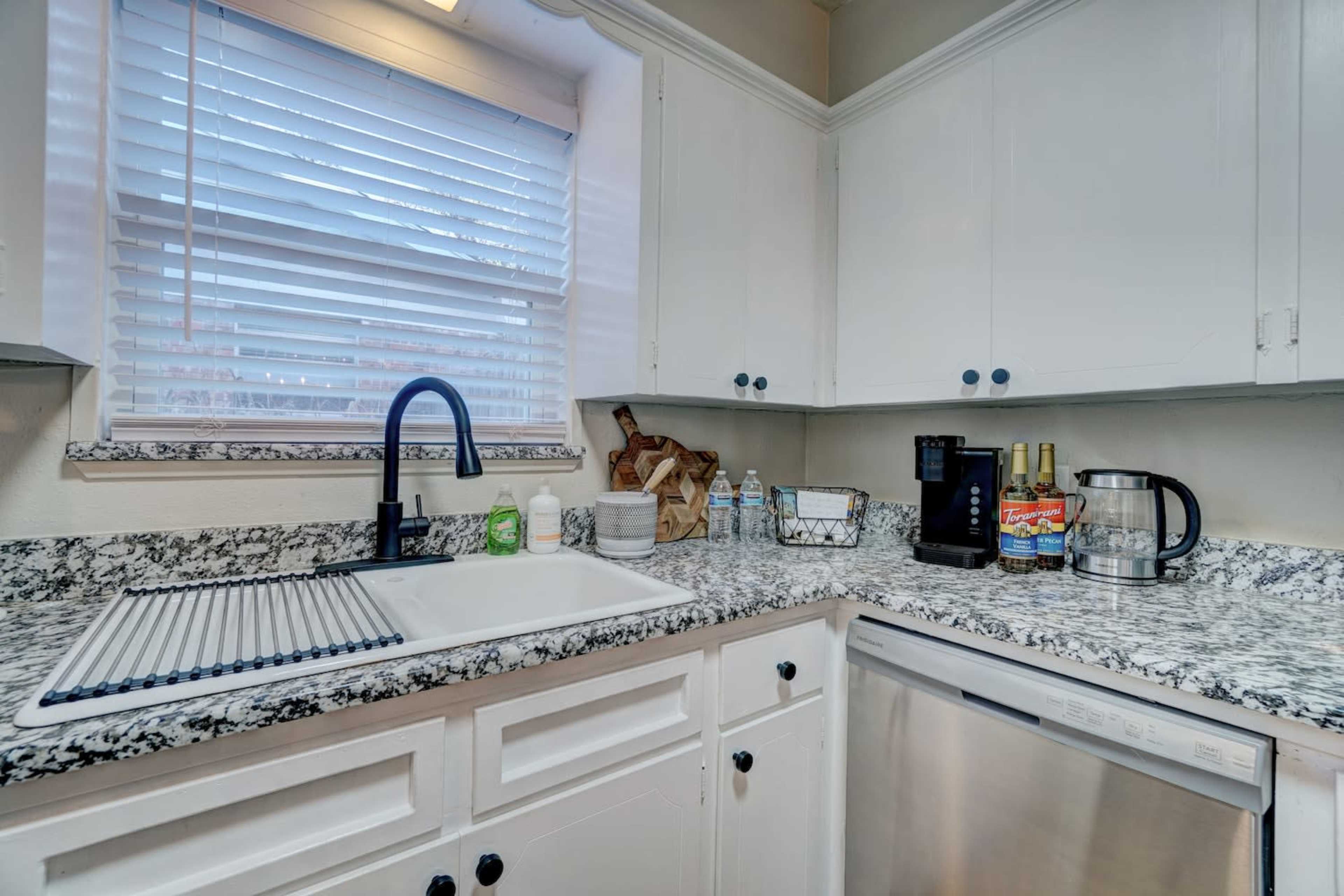 A kitchen featuring white cabinets, a granite countertop, a double sink, and various kitchen appliances including a coffee maker and a kettle.