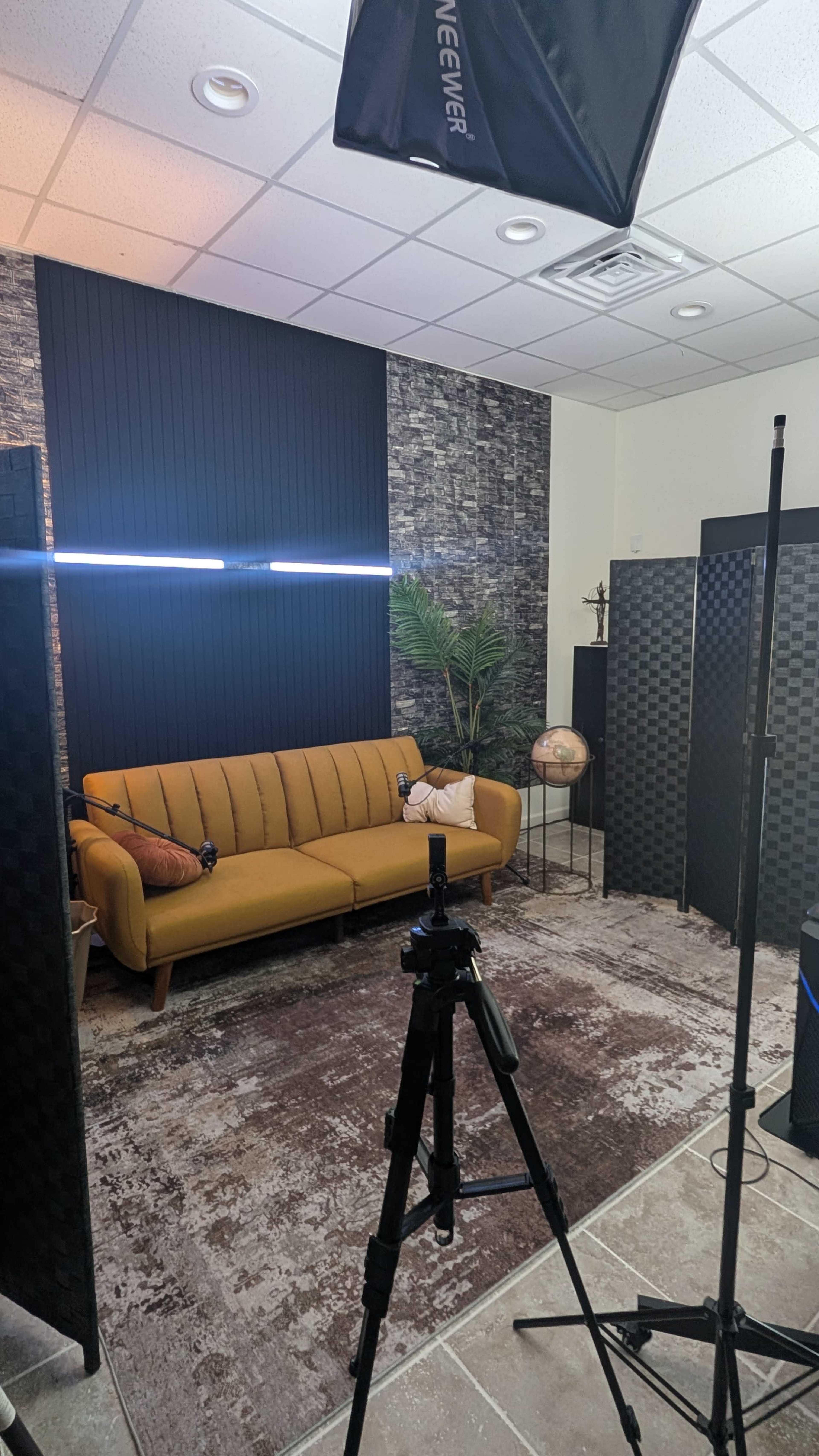 A cozy studio setup features a yellow couch, a globe, and backdrop panels, with lighting equipment positioned for filming.