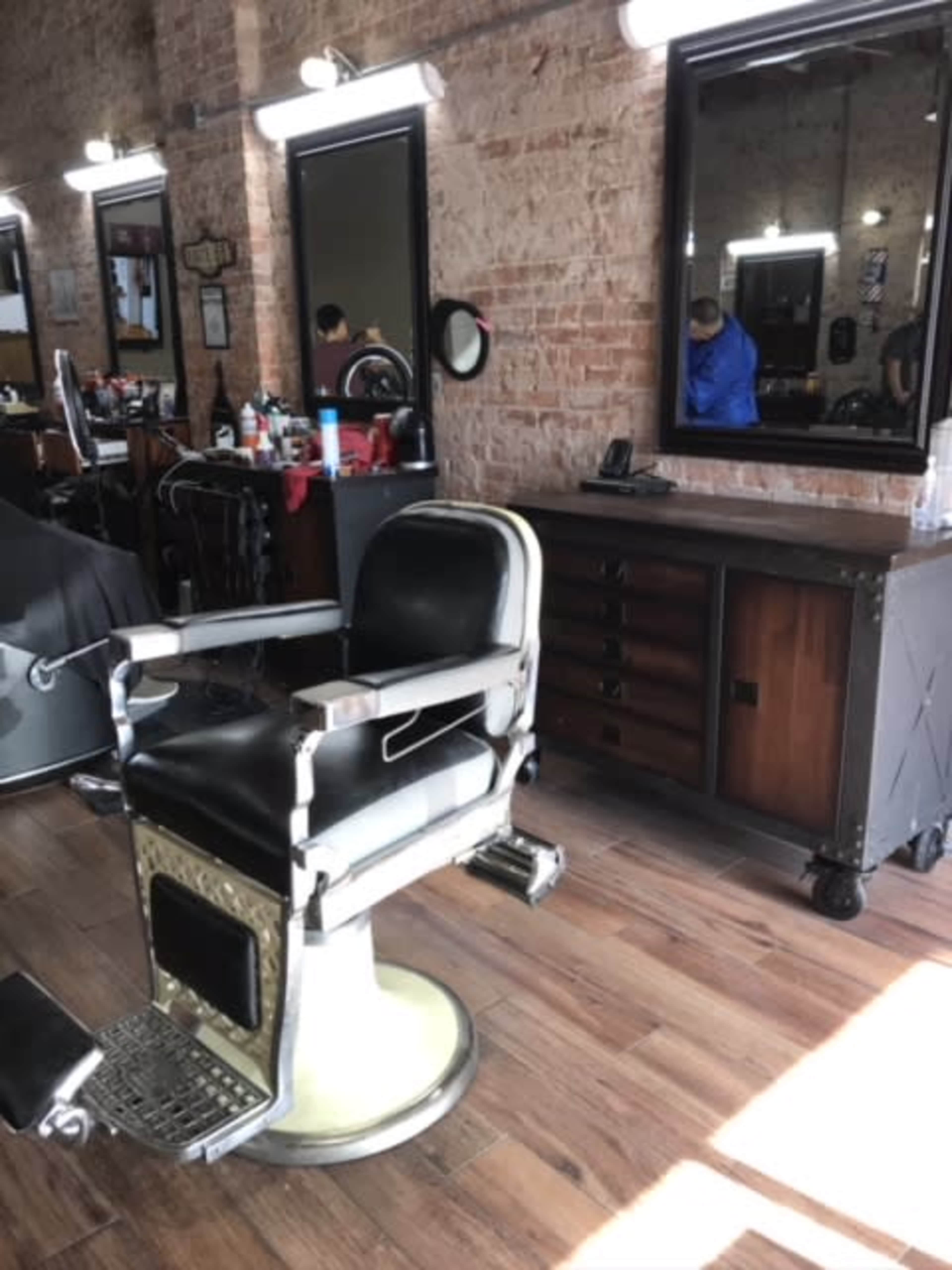 A vintage barber chair in a barber shop with brick walls and wooden flooring, and various grooming products on the counter.