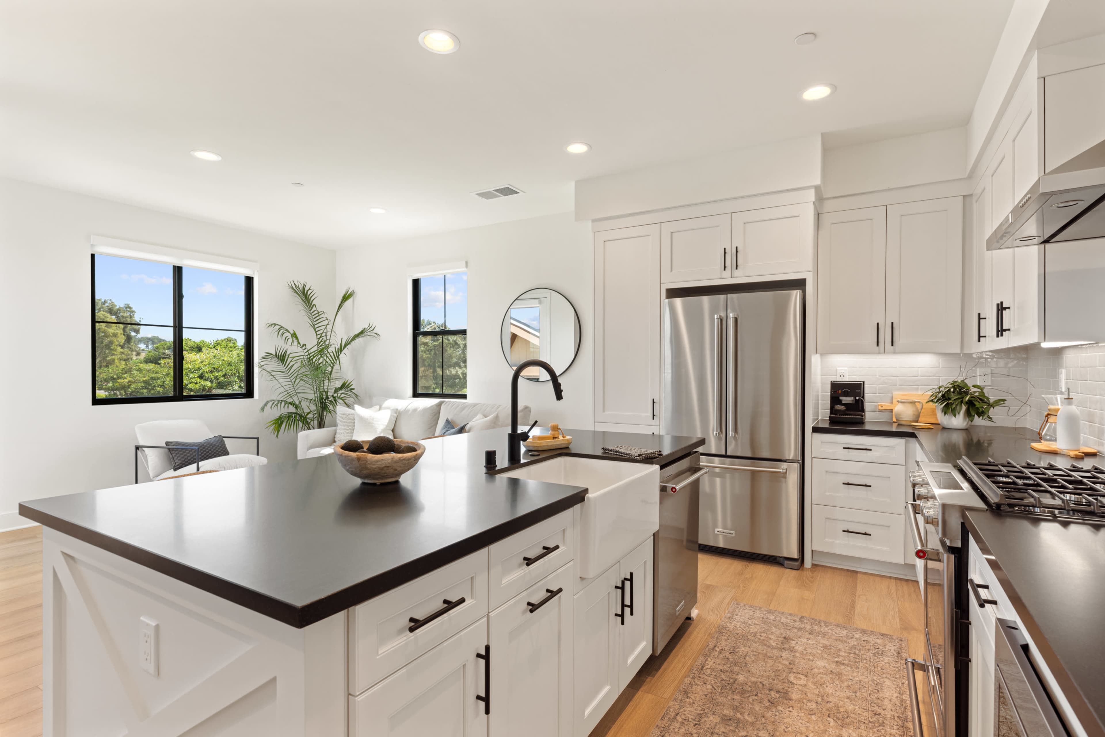 The image shows a modern kitchen featuring white cabinetry, stainless steel appliances, and a large island with a black countertop.