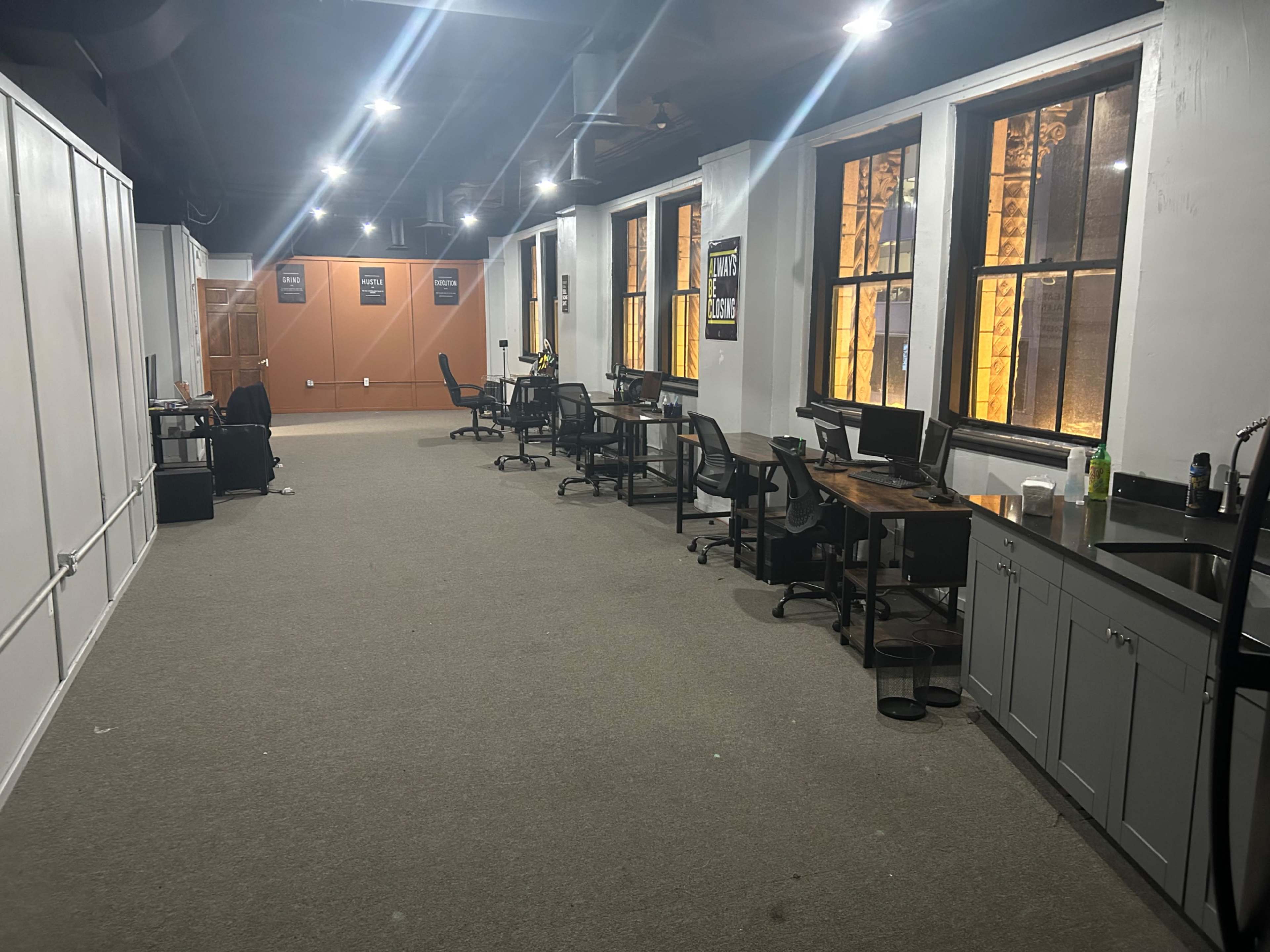A large, empty office space with several desks, computers, and illuminated windows.
