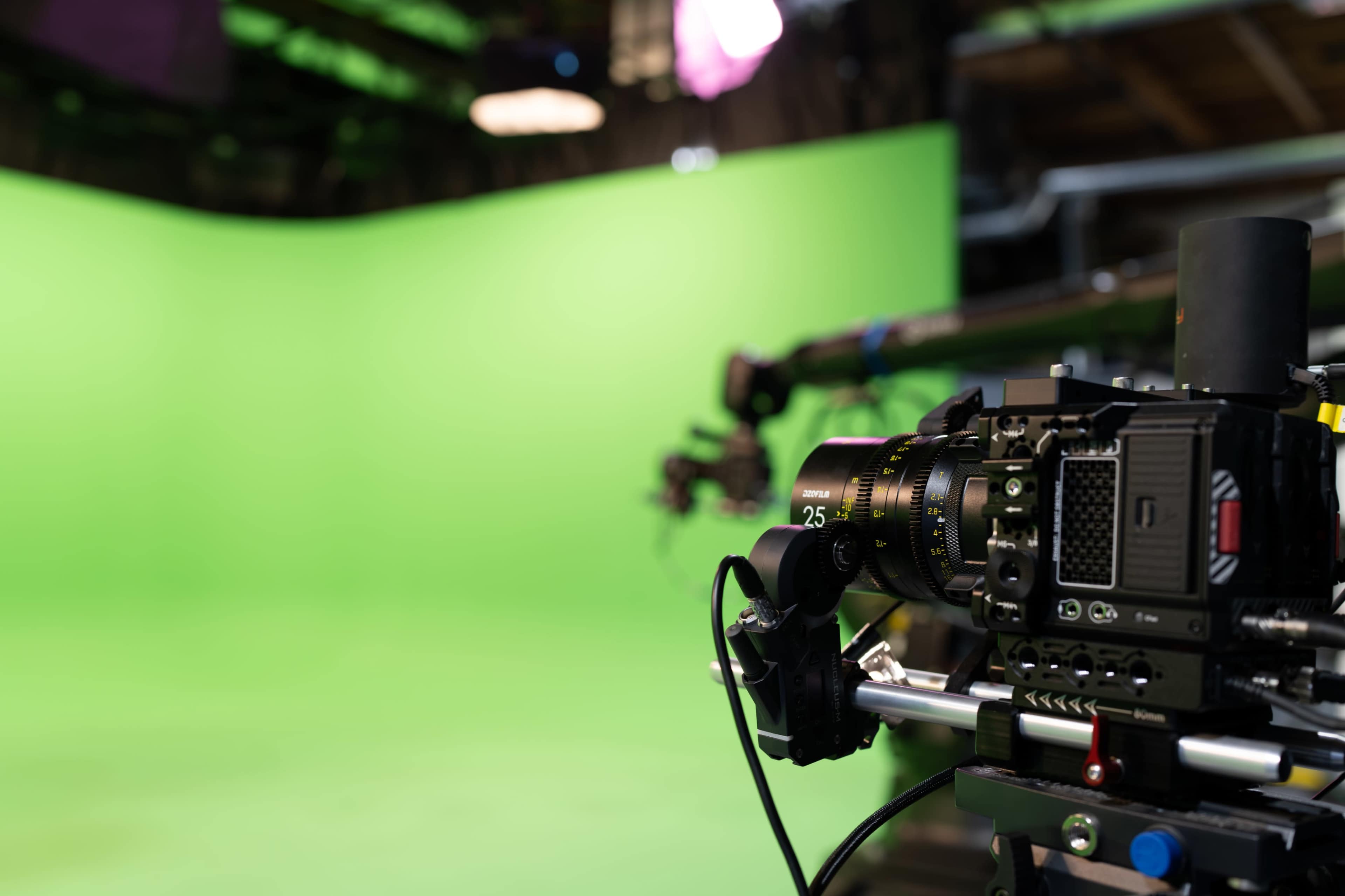 The image shows a film camera set up in a studio with a green screen in the background.