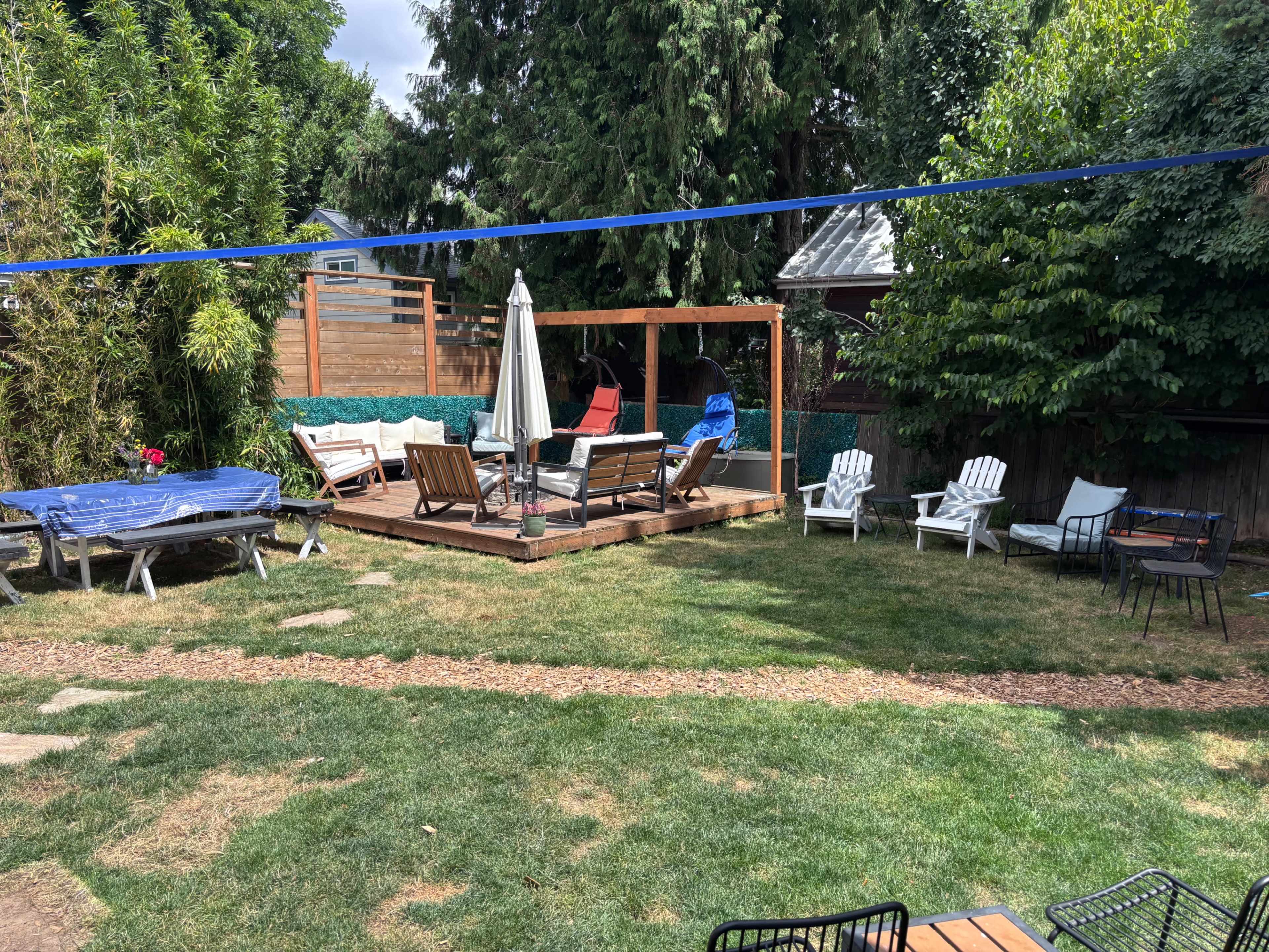 The image shows a backyard with a wooden deck, various seating options including lounge chairs and a table, green grass, and a laundry line overhead.