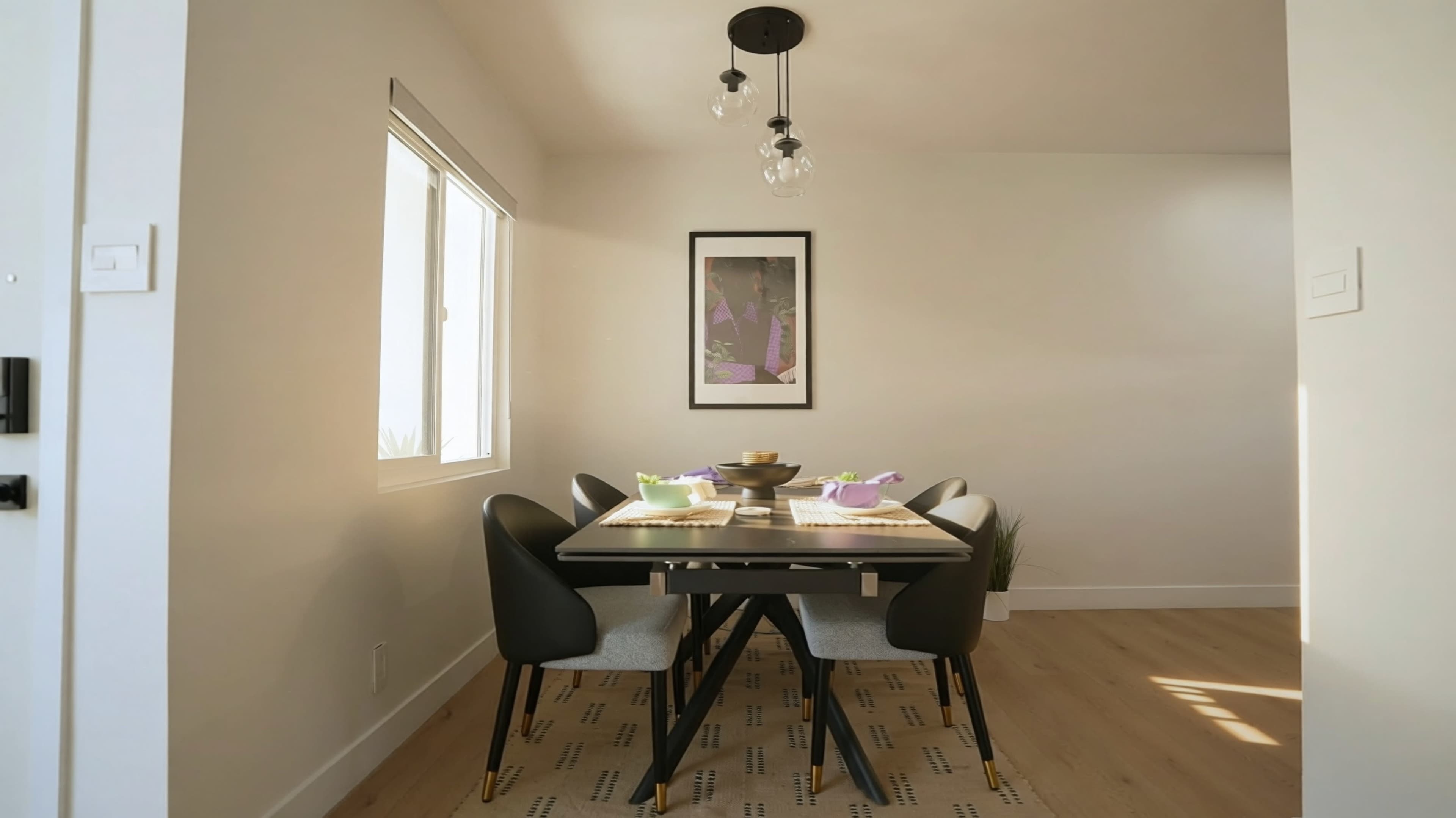 A modern dining area features a table set for meals, surrounded by chairs, with large windows allowing natural light to enter.