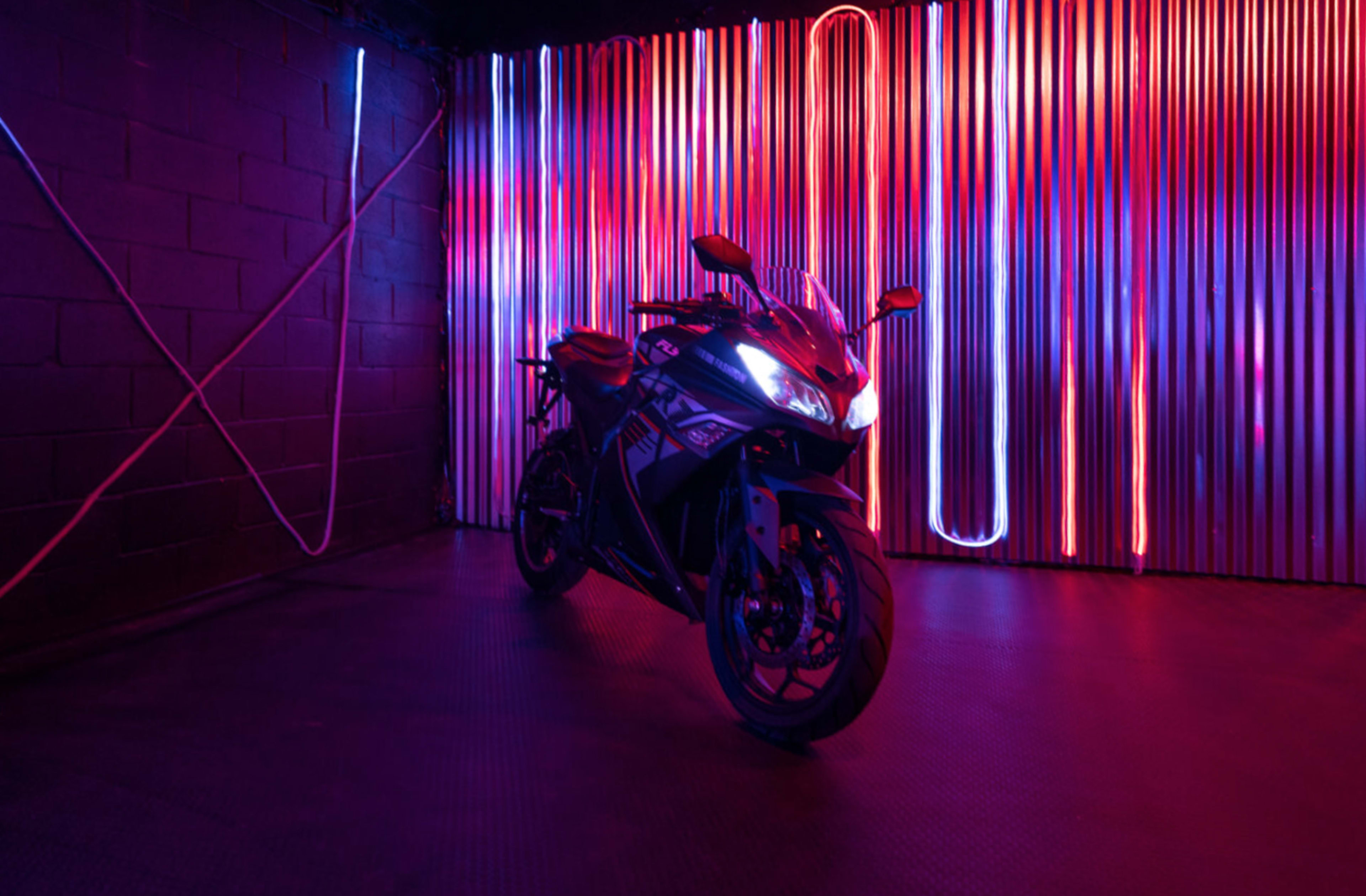 A motorcycle is positioned in front of illuminated vertical panels emitting red and blue light in a dark room.