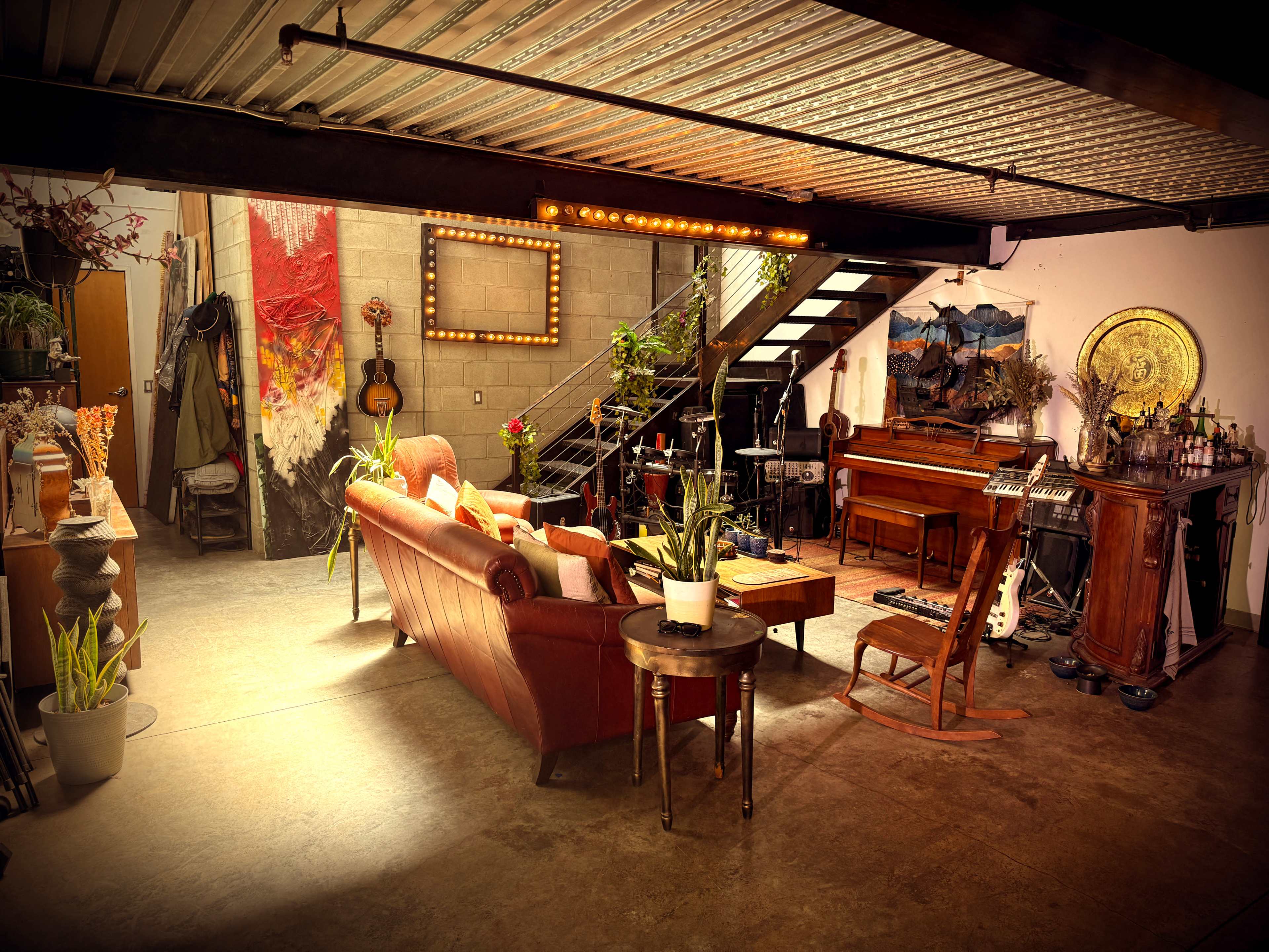 The image shows a spacious, industrial-style living area featuring a red couch, a wooden piano, and various plants, with a staircase leading to an upper level.