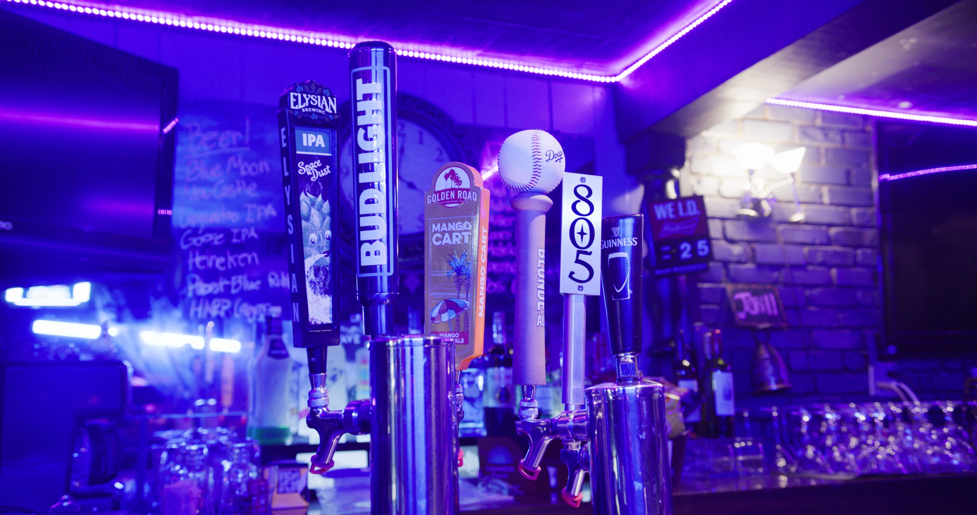 A row of beer taps at a bar, showcasing various brands including Bud Light, Elysian IPA, and 805, with a baseball resting on one of the taps.