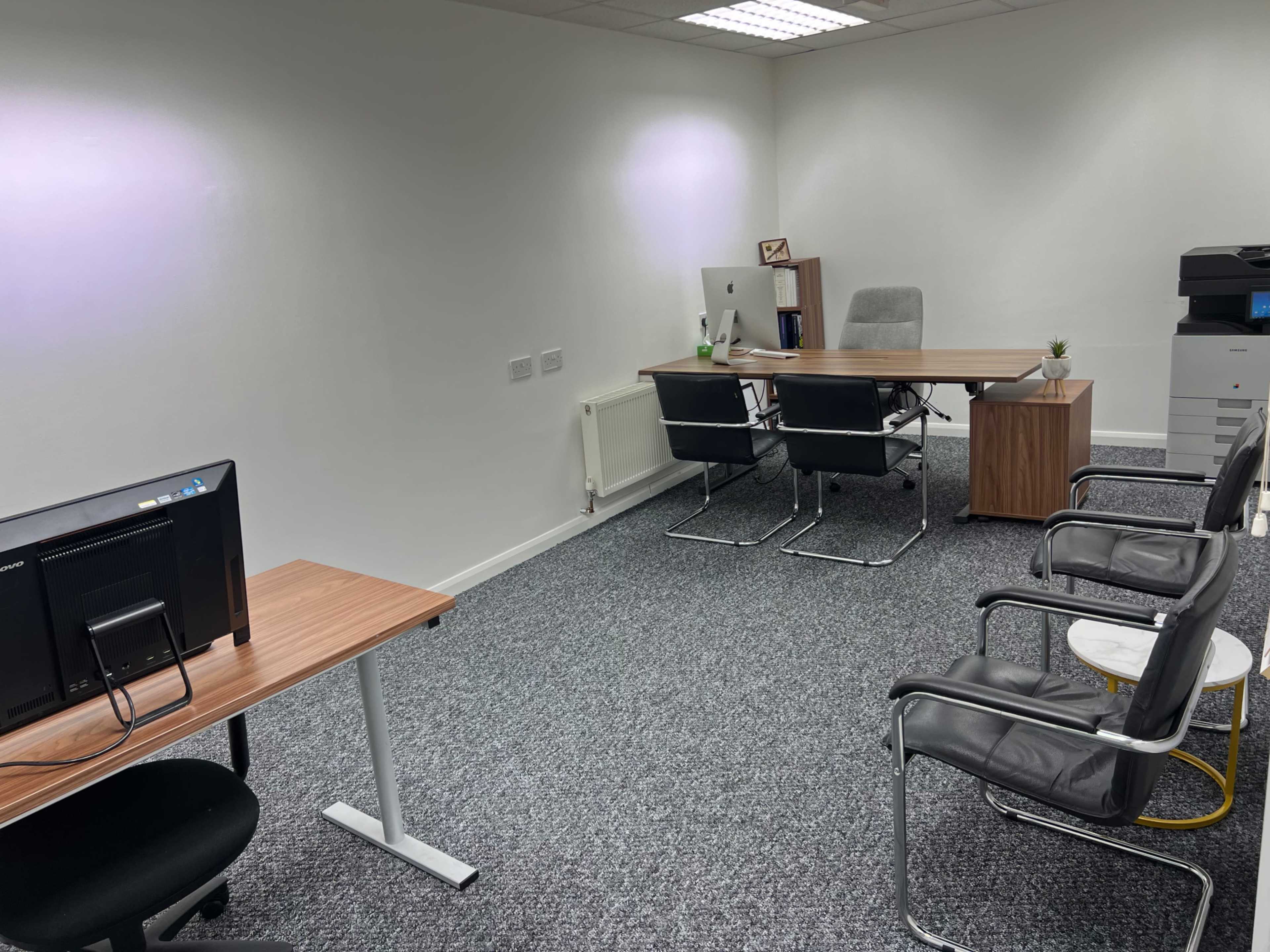 The image shows an office space with two desks, several chairs, a meeting table, and a printer in the corner.